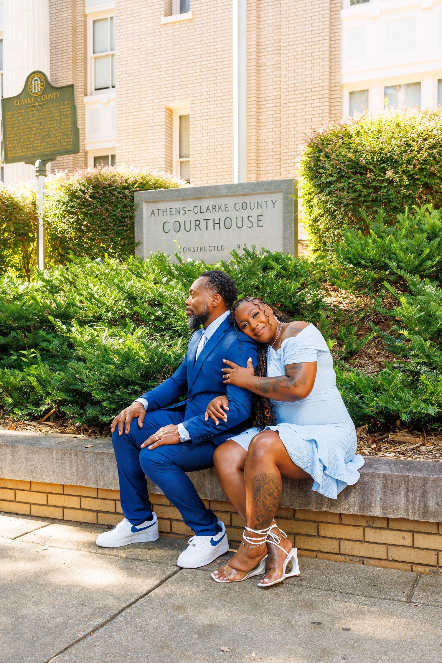 Couple in coordinating blue outfits posing at Athens-Clarke County Courthouse sign outdoors.