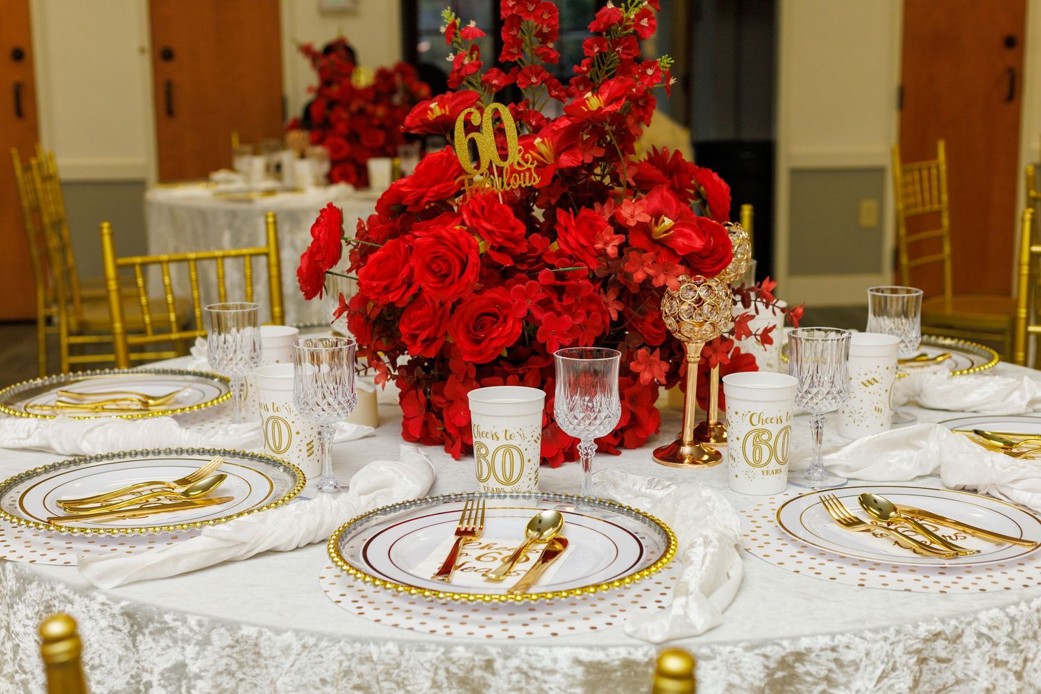Elegant 60th birthday table setting with red roses, gold chargers, and crystal glassware.