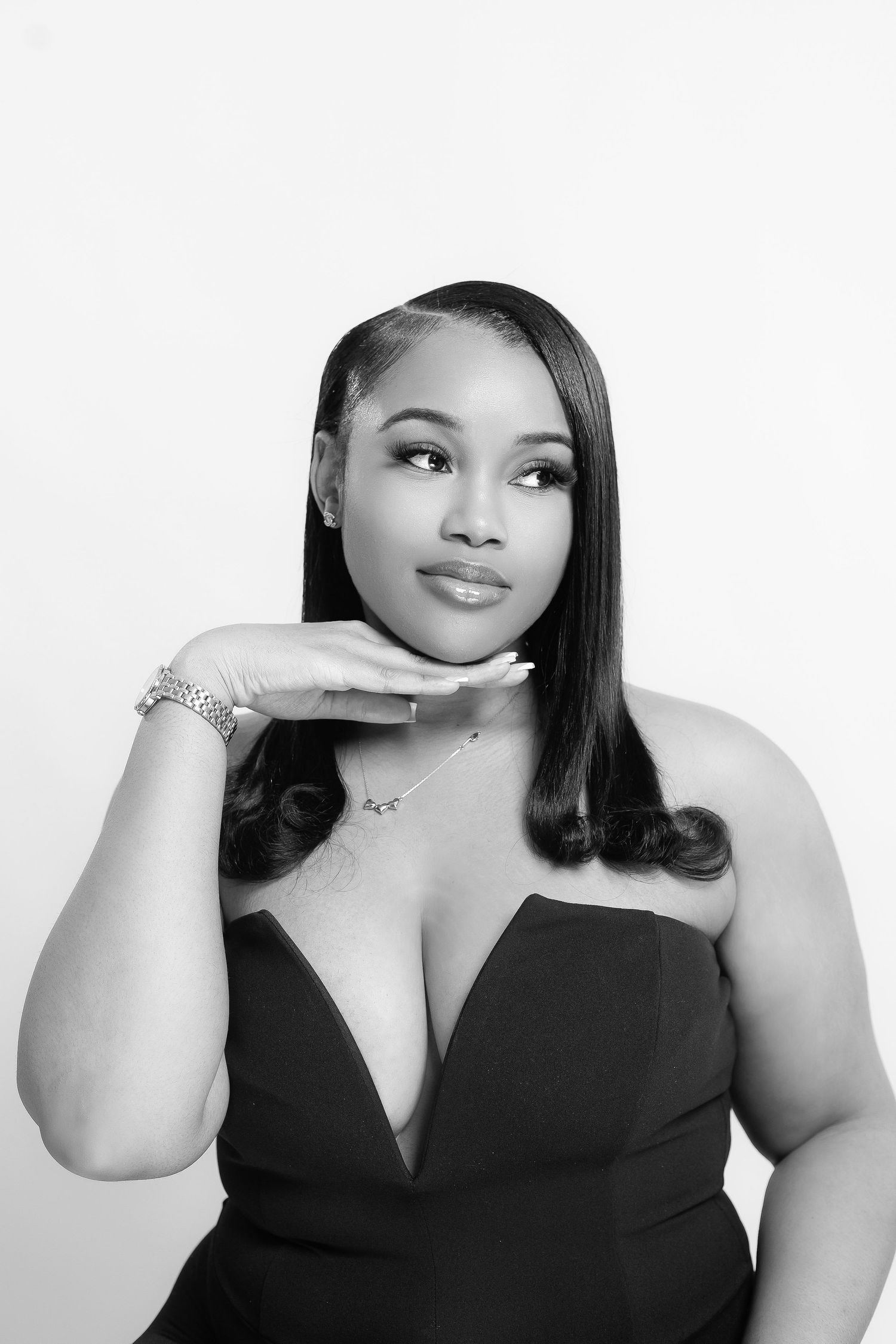 Black and white portrait of a young woman in a strapless dress, posing thoughtfully with hand near chin.
