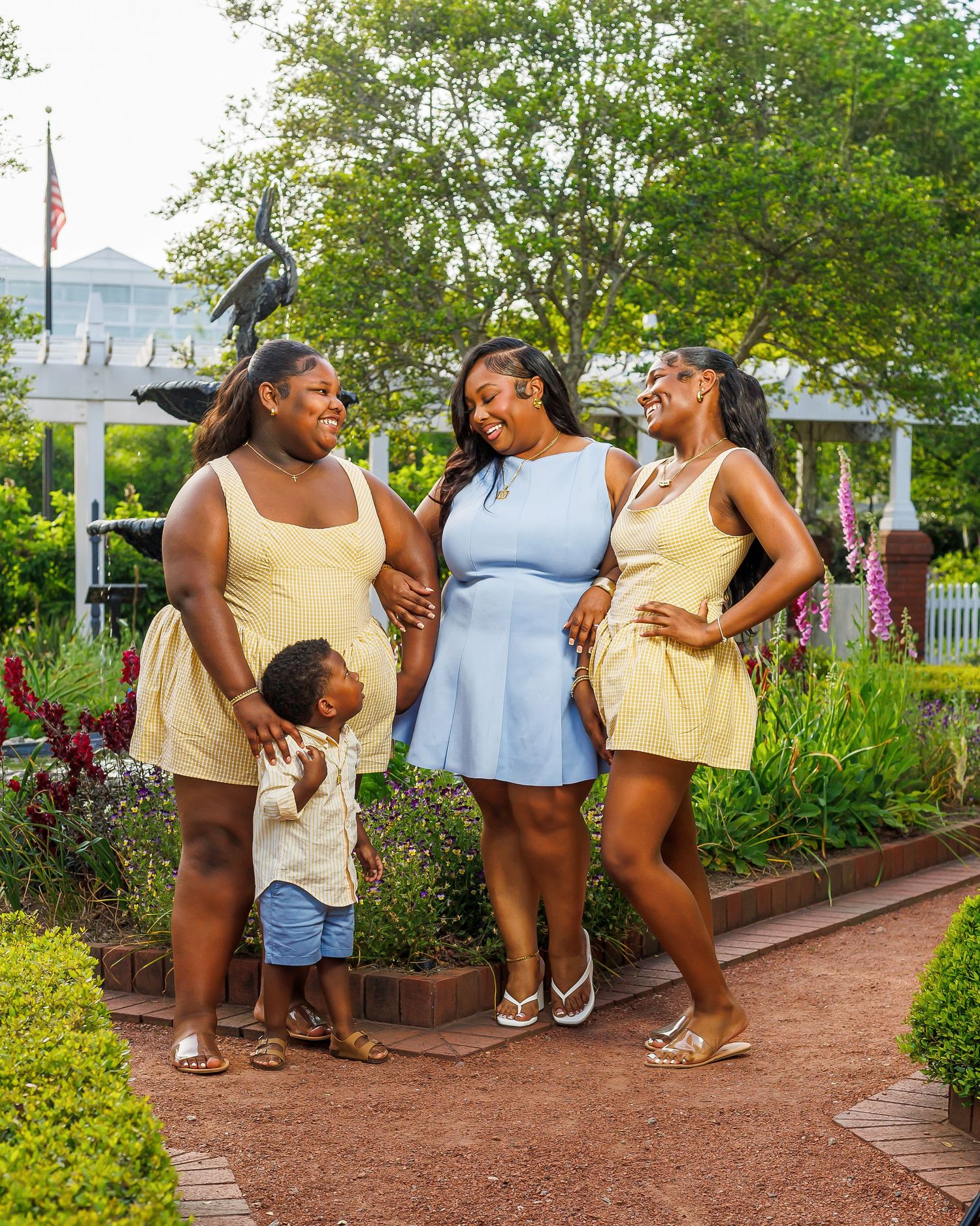 Woman in blue dress with two girls and a toddler posing in a scenic garden pathway.