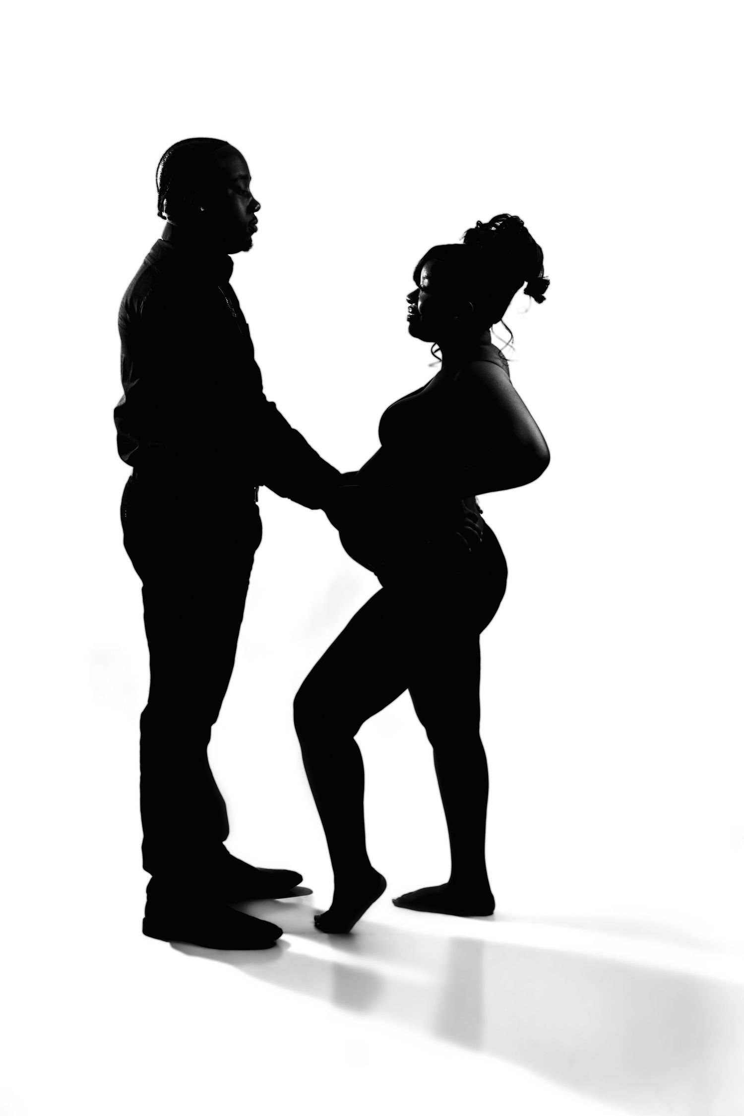 A dramatic black and white silhouette of a pregnant couple holding hands against a white background.