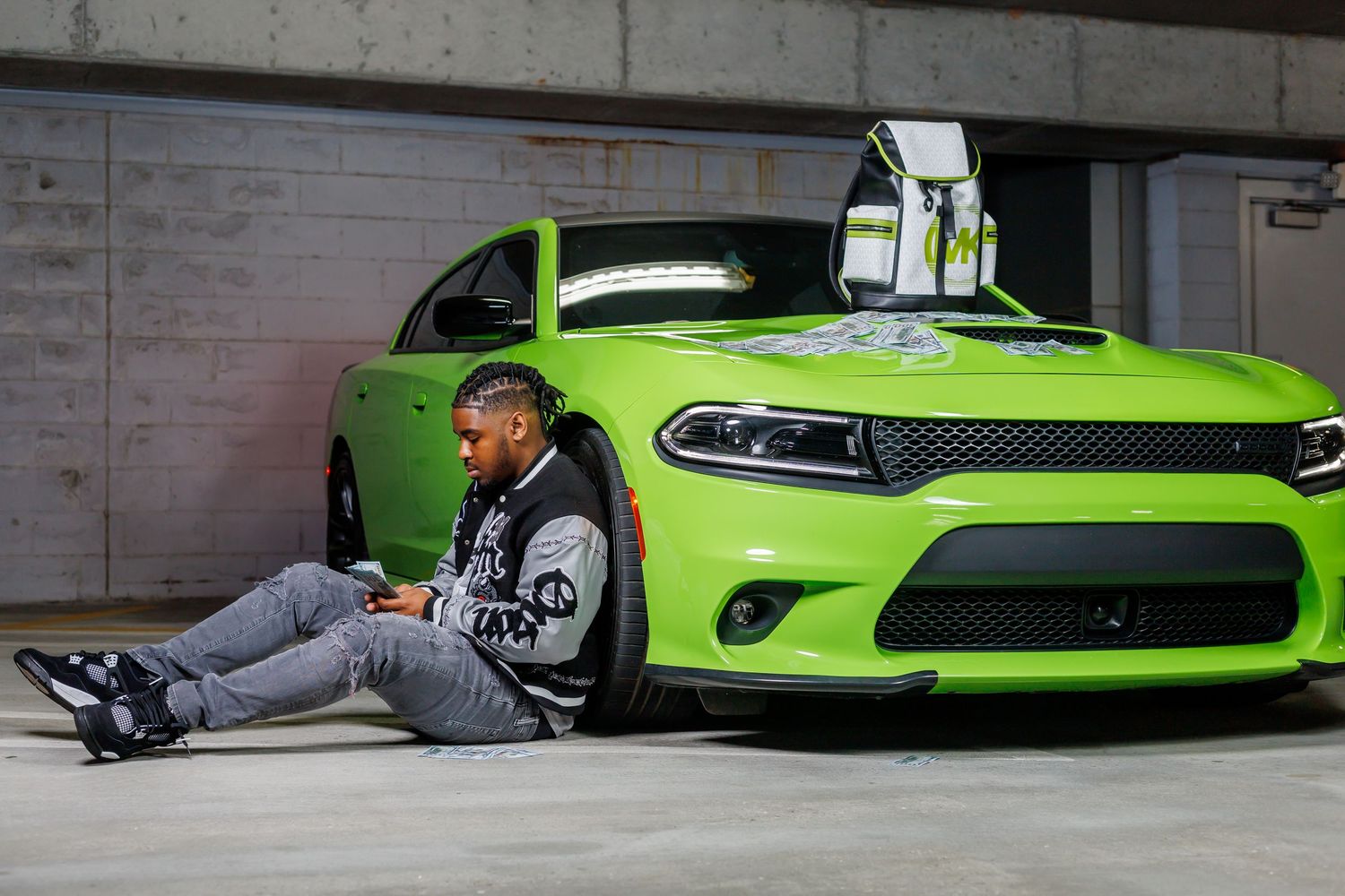 Man sitting against a lime green Dodge Charger in a parking garage, looking at his phone.