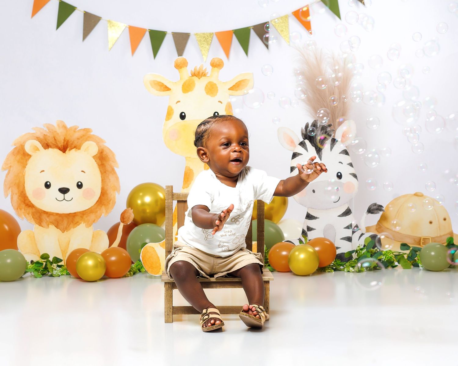 Happy baby in white outfit reaching up during safari-themed first birthday cake smash session.