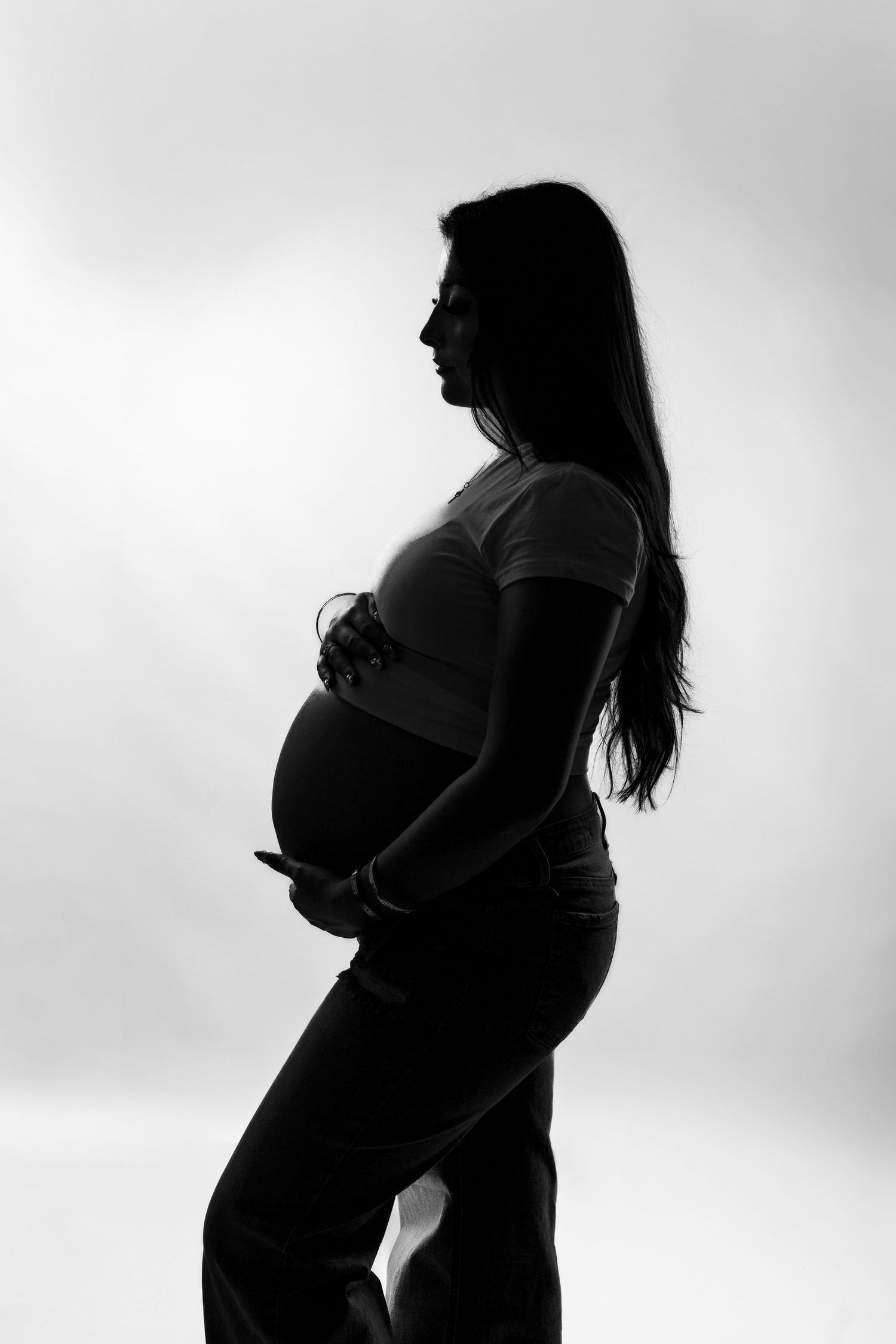Black and white silhouette of a pregnant woman cradling her baby bump against a light background.