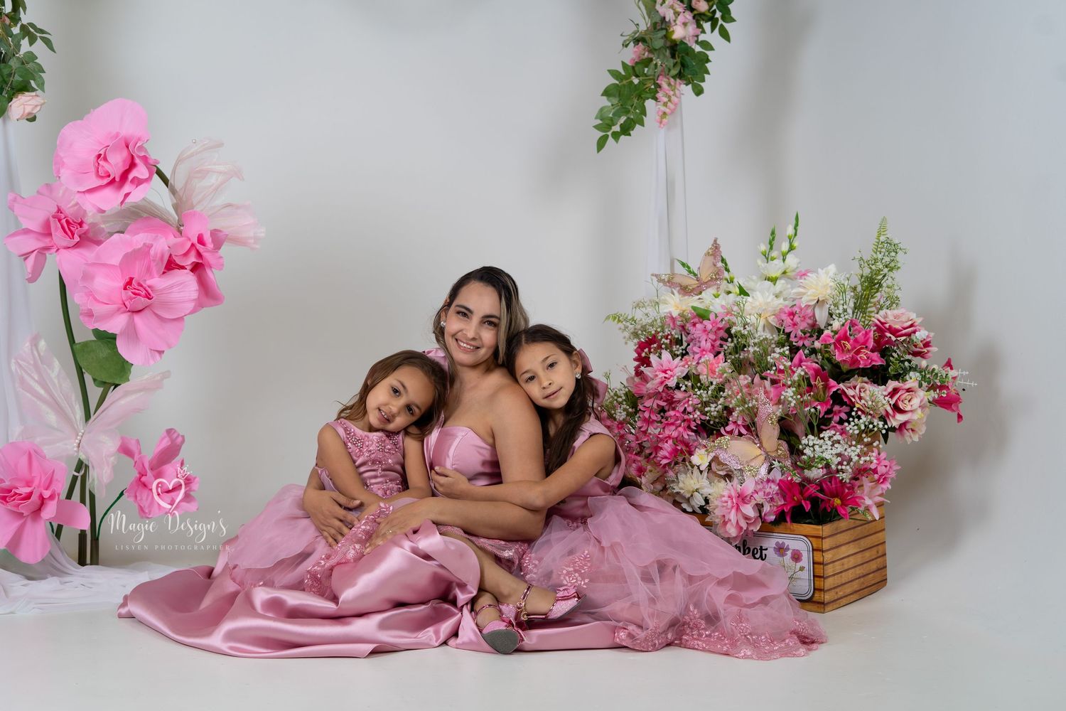 A touching portrait session featuring pink satin dresses and floral decorations against a white backdrop.