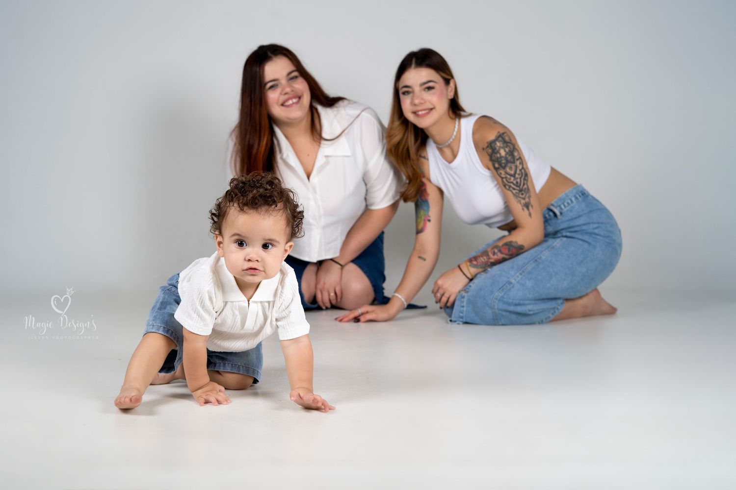 Family lying together on white studio floor in casual clothing.