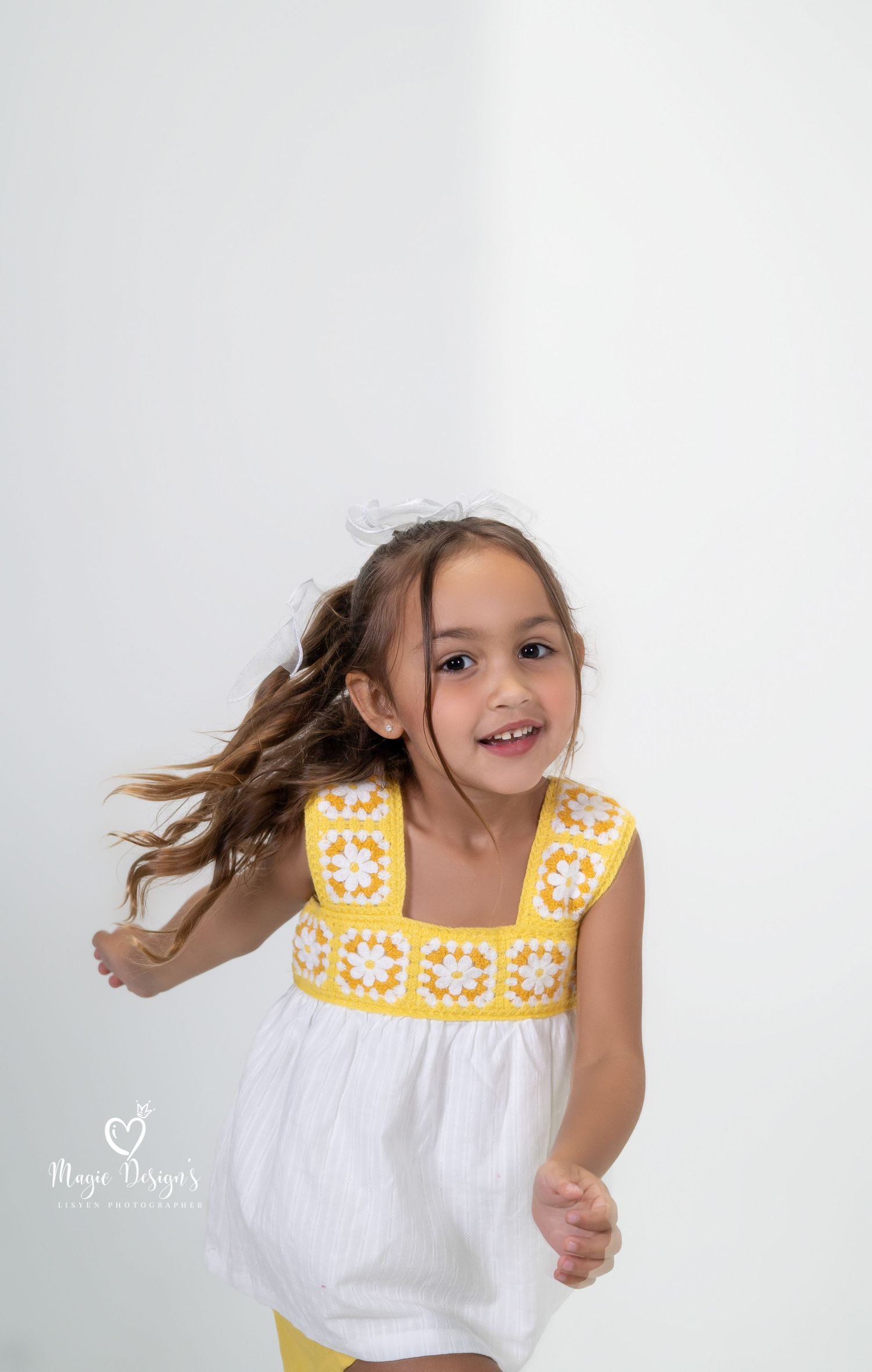 Young girl in white and yellow dress twirling and dancing against white backdrop.