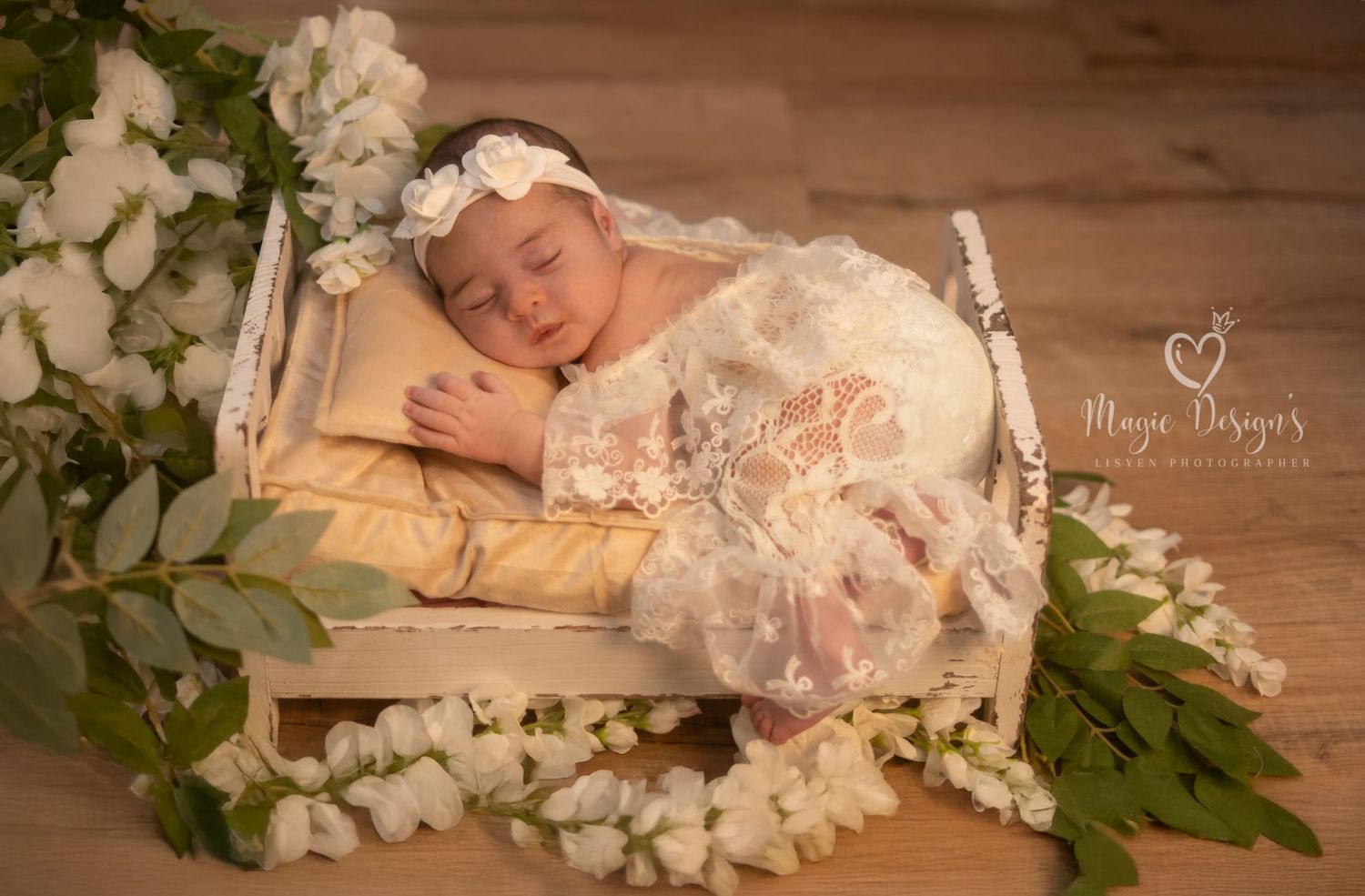 Dreaming baby surrounded by white flowers and greenery in rustic wooden setting.