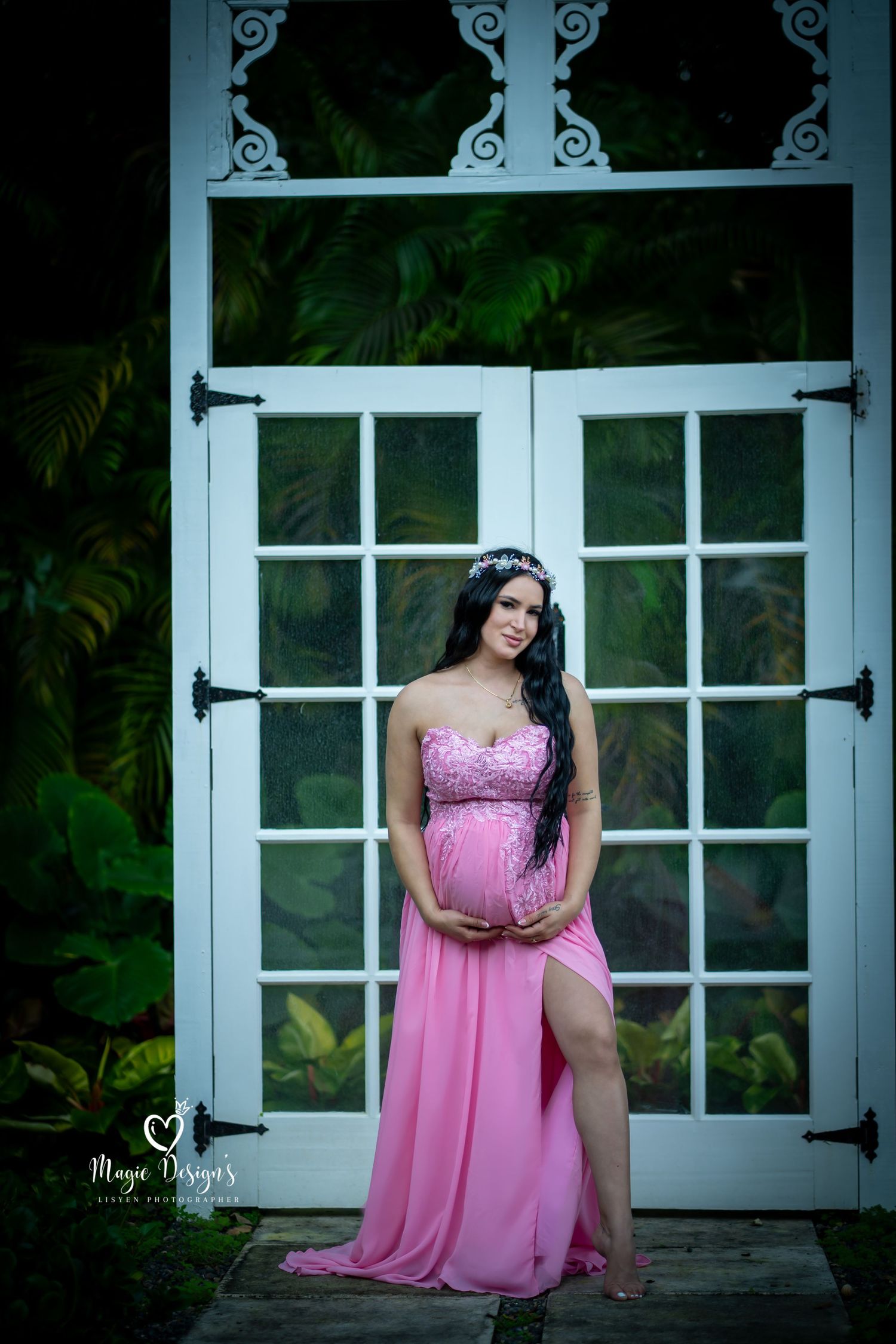 Maternity photoshoot in a garden setting with white shuttered windows and a flowing pink dress.