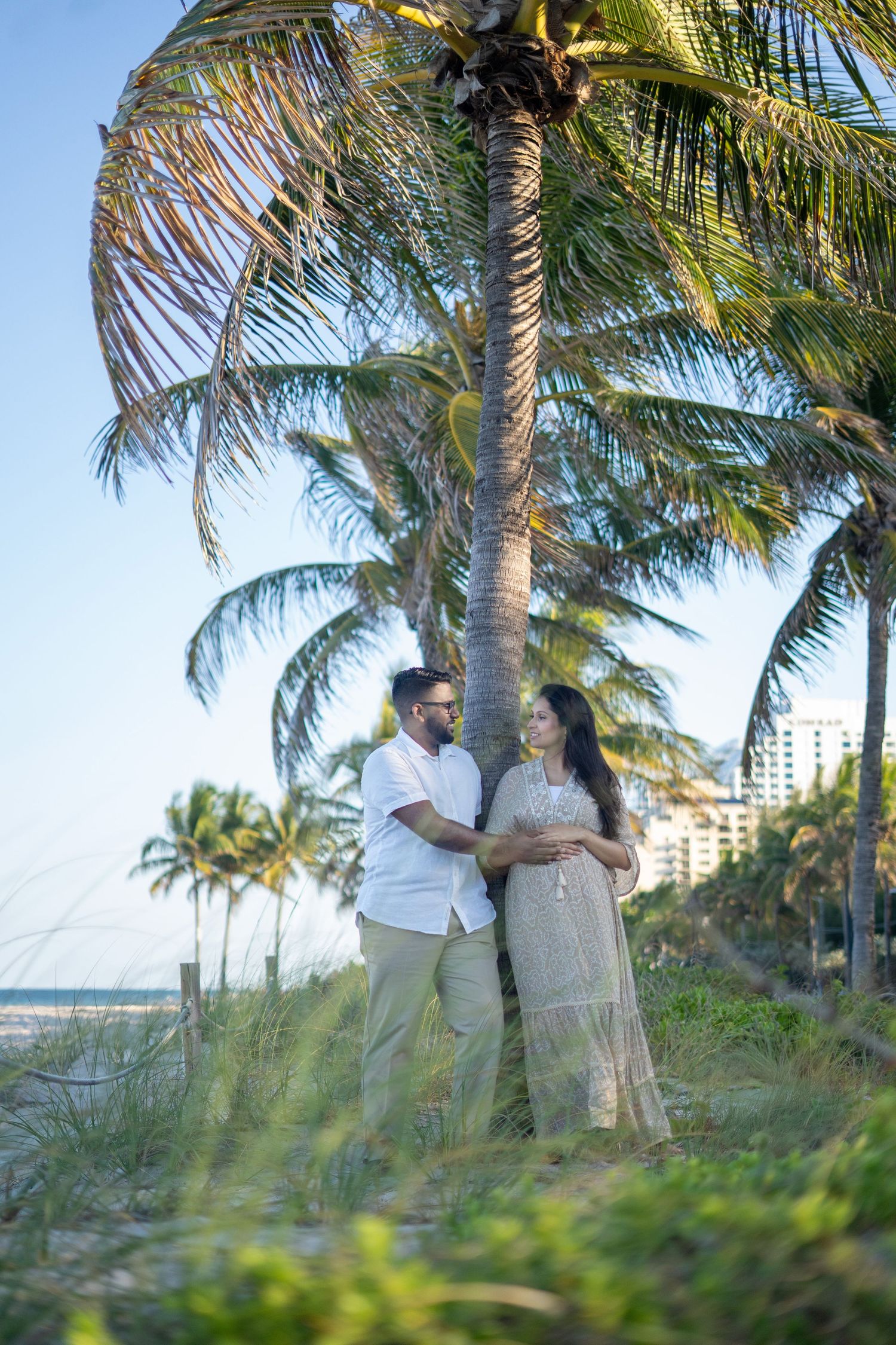 A romantic couple shares a tender moment under swaying palm trees on a tropical beach at sunset.