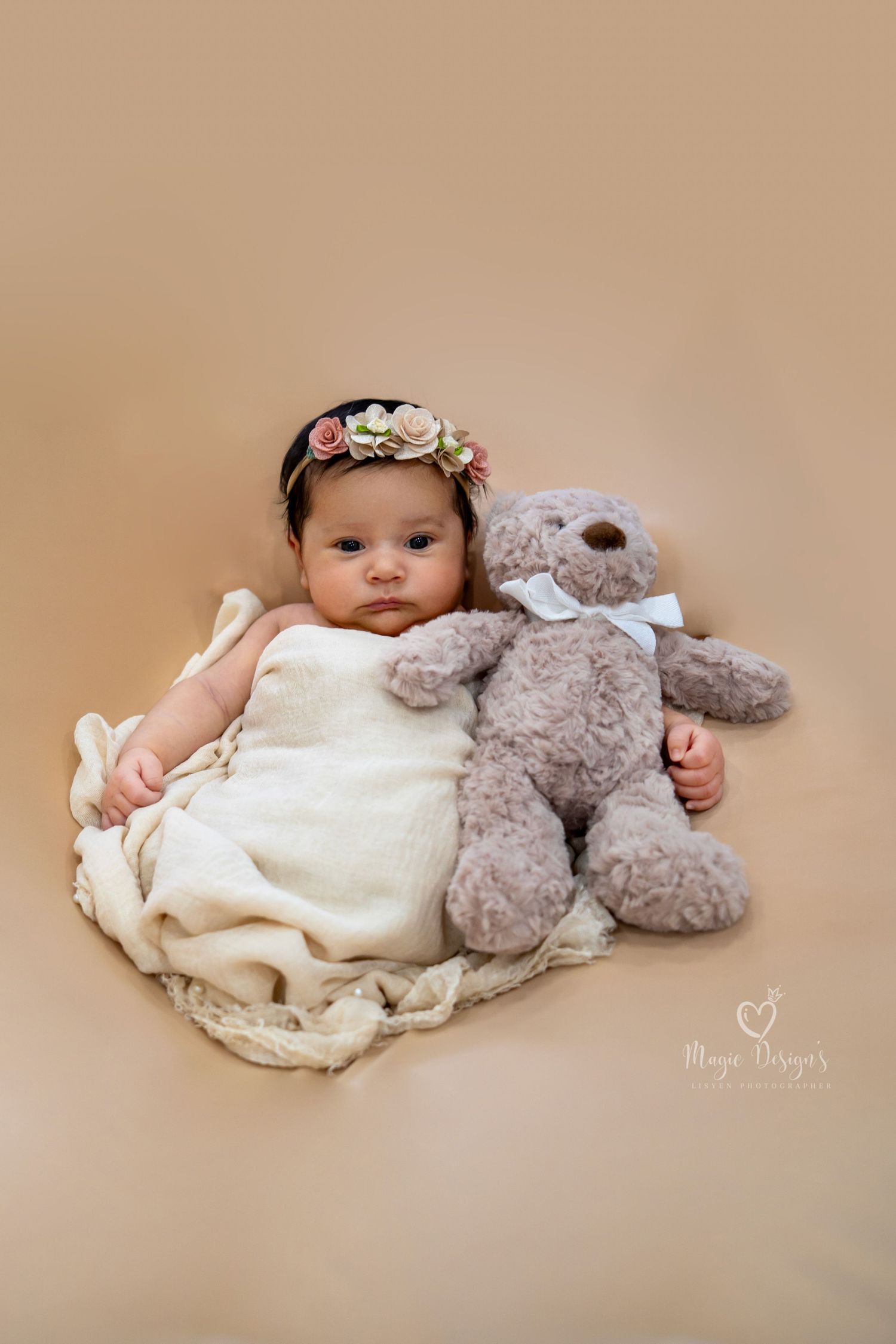 Sweet newborn portrait with plush grey teddy bear and cream-colored outfit.