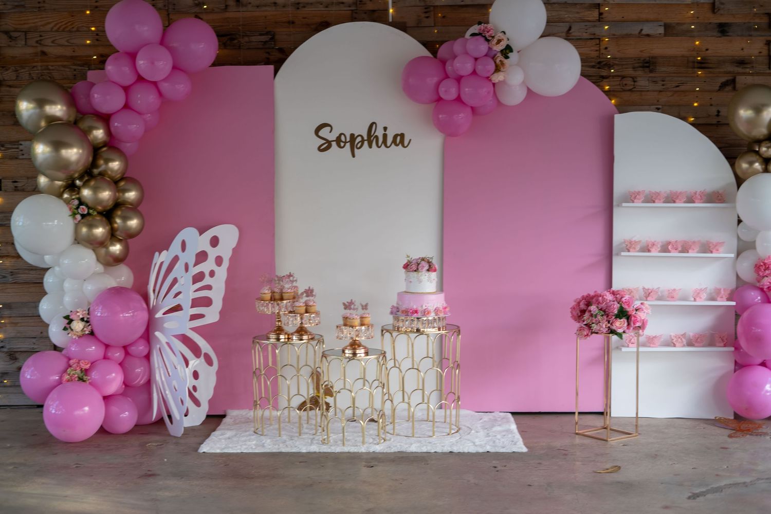 Pink and white balloon decorations with butterfly accents create an elegant party backdrop for a special celebration.