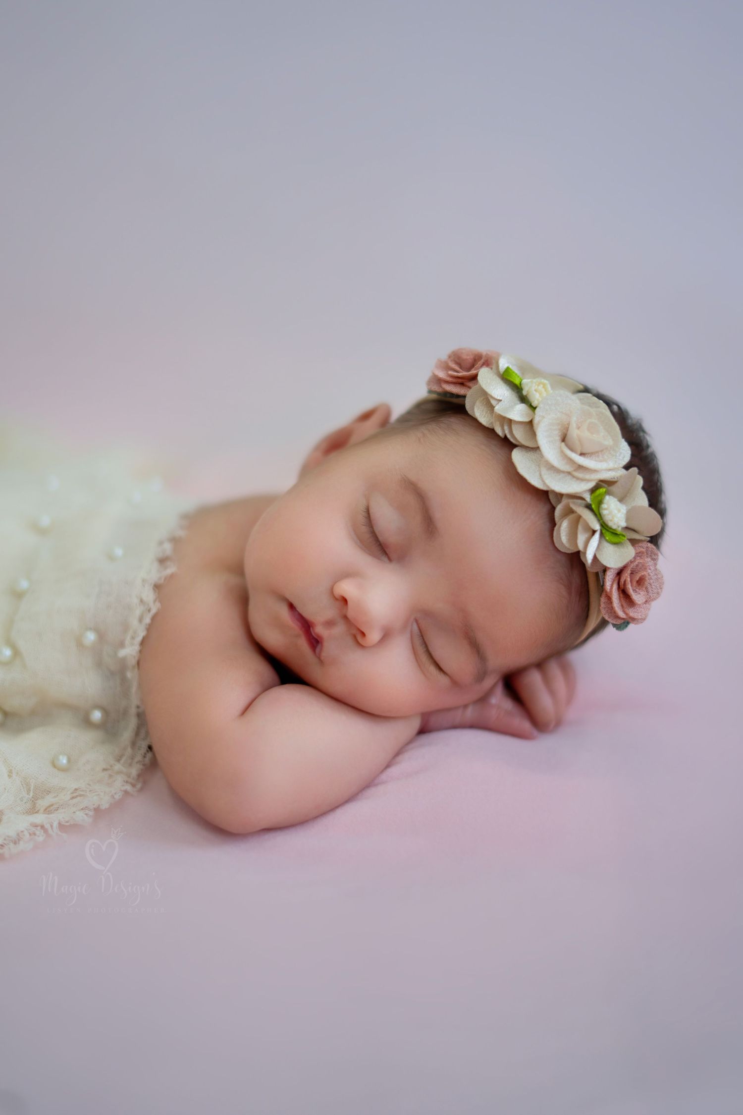 Peaceful newborn wearing floral headband and lace dress on pink backdrop.