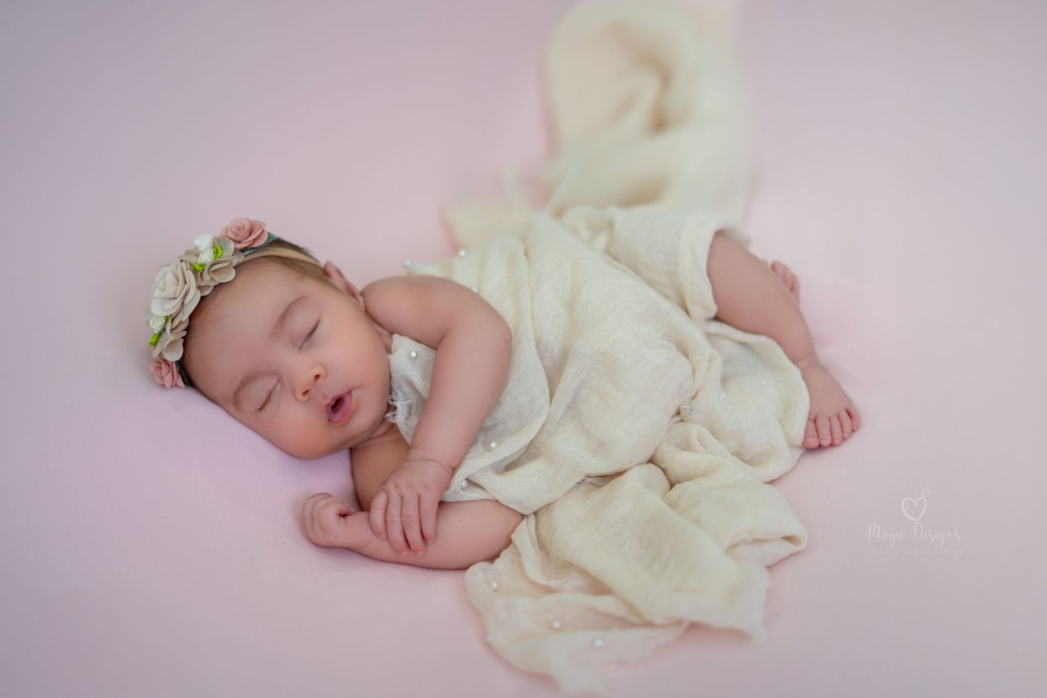 Sleeping infant in cream-colored dress against soft pink background.