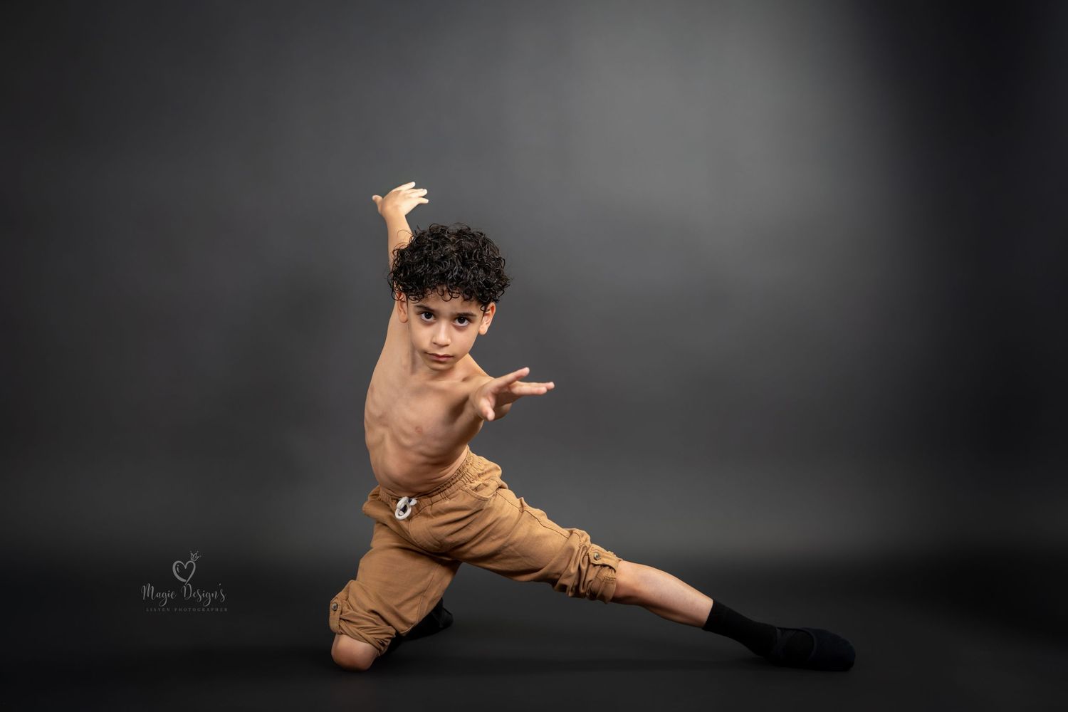 Dancer in brown outfit performs dramatic martial arts inspired pose against dark background.
