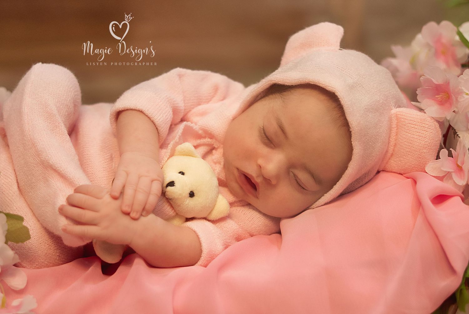 Sweet newborn baby sleeping on pink blanket with small teddy bear in soft lighting.
