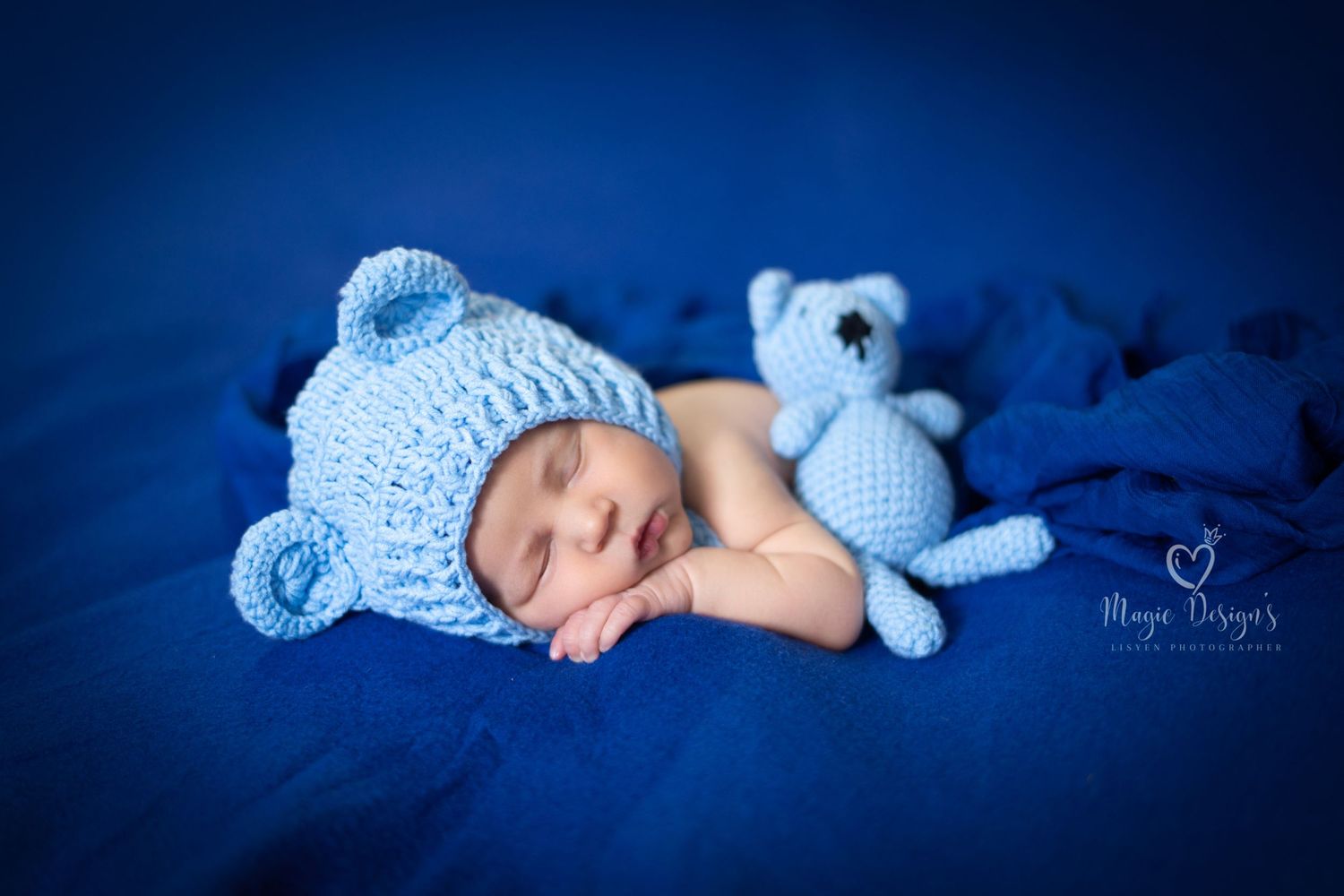 Sleeping newborn wearing blue knit hat with stuffed toy in blue-toned portrait series.