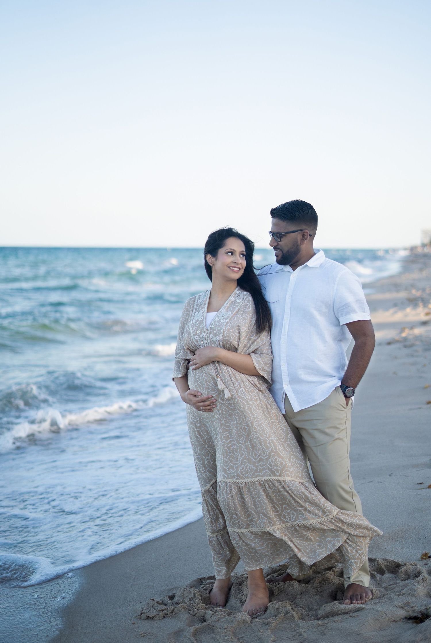 A couple shares a romantic moment on a sandy beach at sunset as waves roll in along the shoreline.