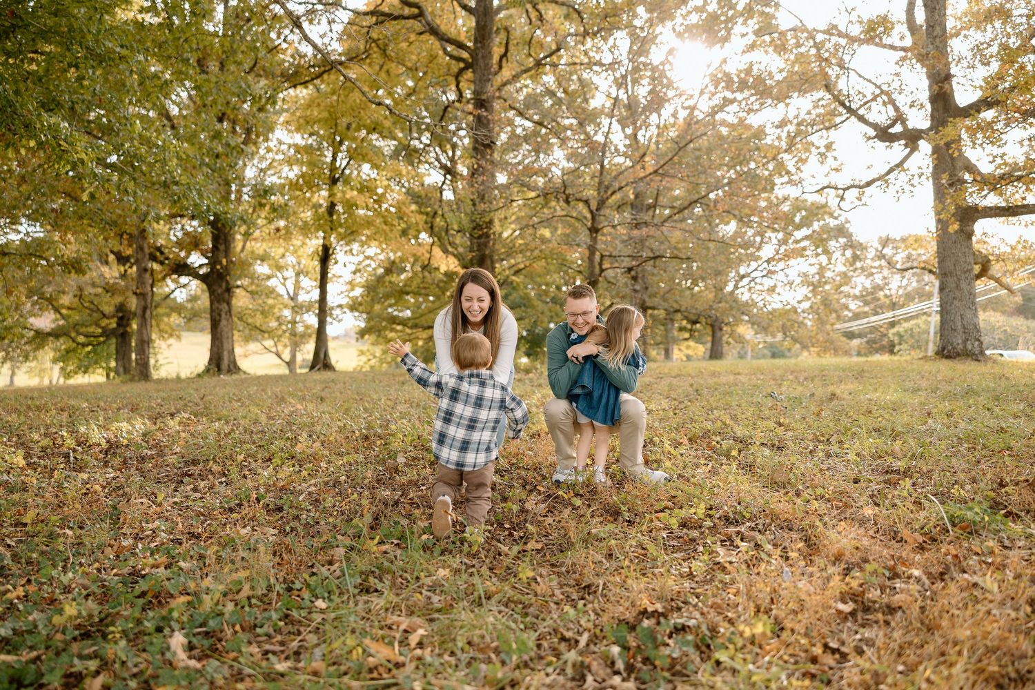 Two children playing and running through a scenic autumn park with golden fall foliage and tall oak trees.