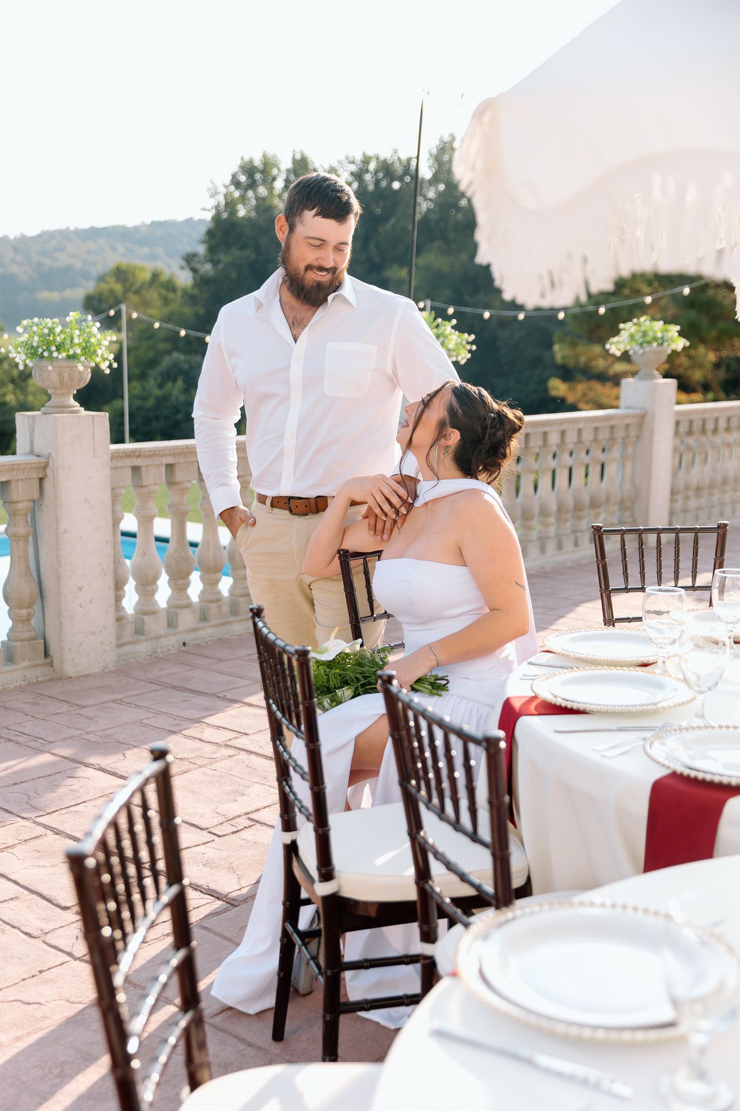 Bride and groom share a tender moment at an elegantly set outdoor wedding reception table on a sunlit terrace.