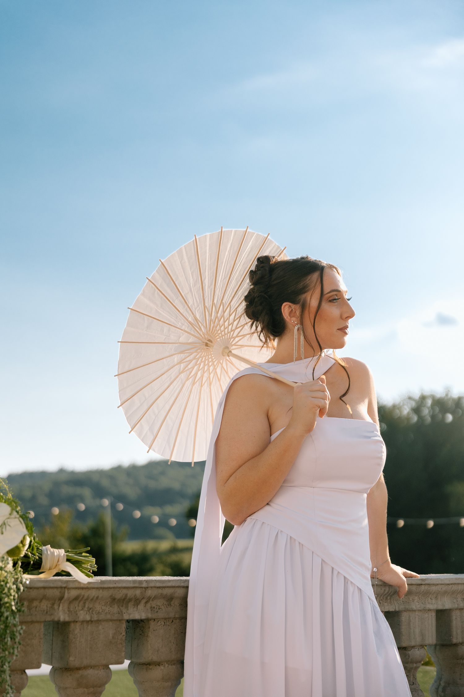 Woman in white dress holding a paper parasol umbrella outdoors on a sunny day with blue sky background.
