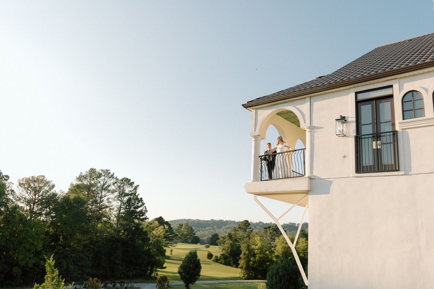 Couple embracing on elegant white balcony overlooking lush green golf course at a wedding venue.
