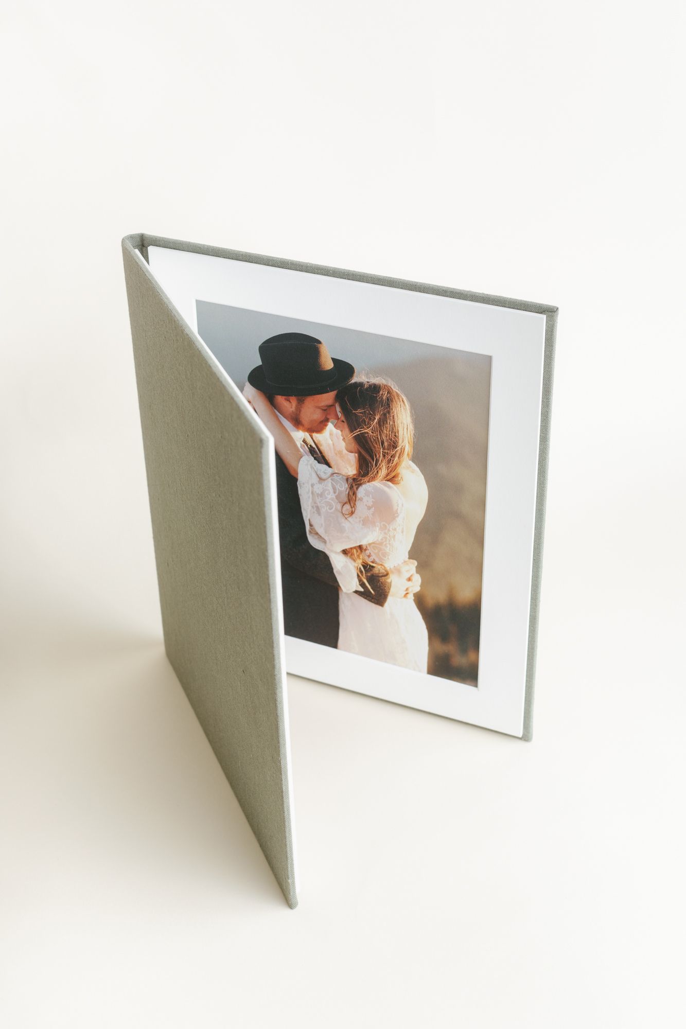 Sage green linen photo album open displaying a romantic couple embracing outdoors, perfect for wedding memories.
