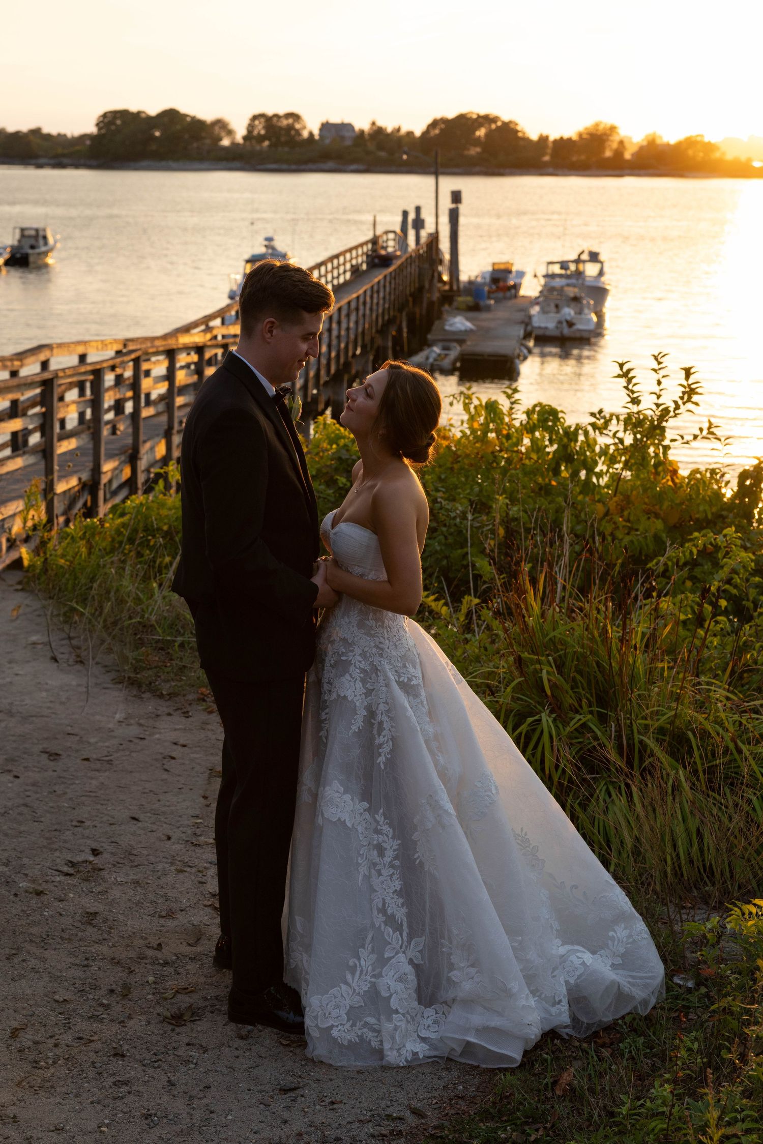 Silhouetted wedding couple embraces by waterfront dock at sunset.