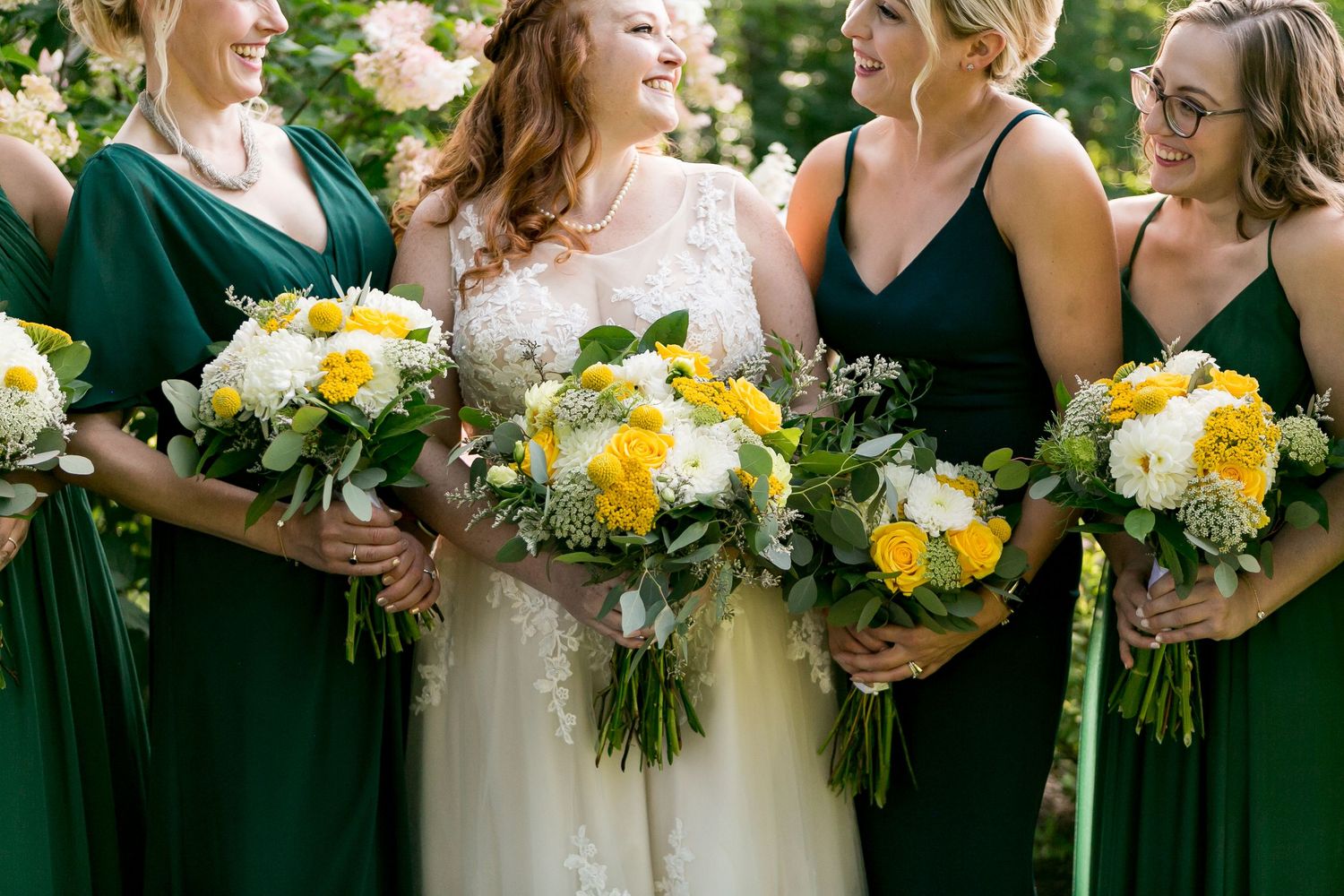 Wedding party holding yellow and white bouquets while wearing emerald green dresses.