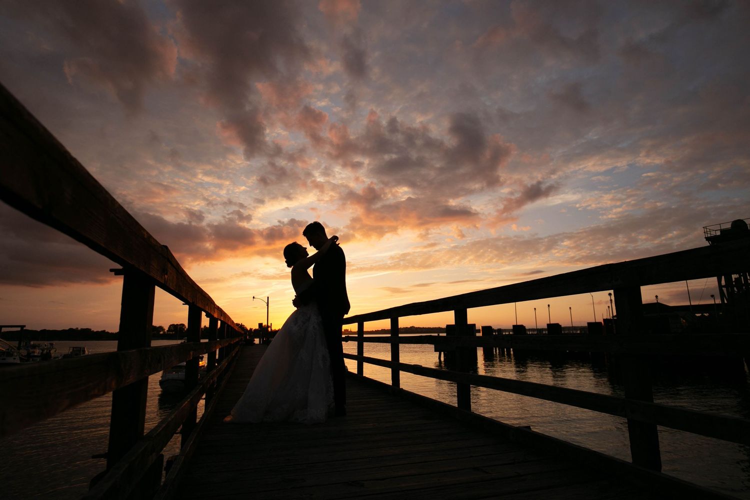 Dramatic orange and purple sunset sky over waterfront with couple in silhouette.