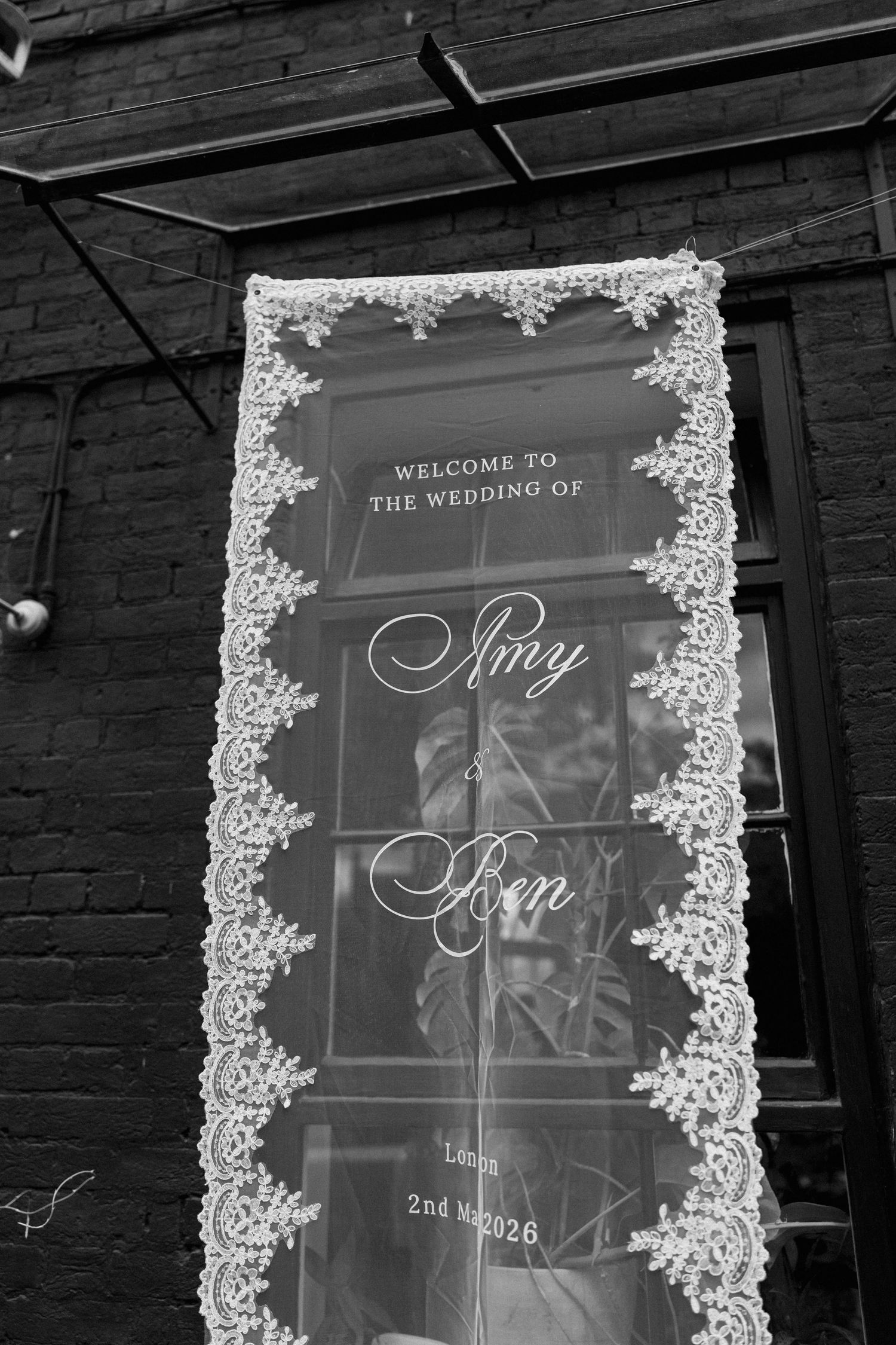 Black and white wedding welcome sign for Amy and Ben, London, 2nd May 2026, framed with lace border.