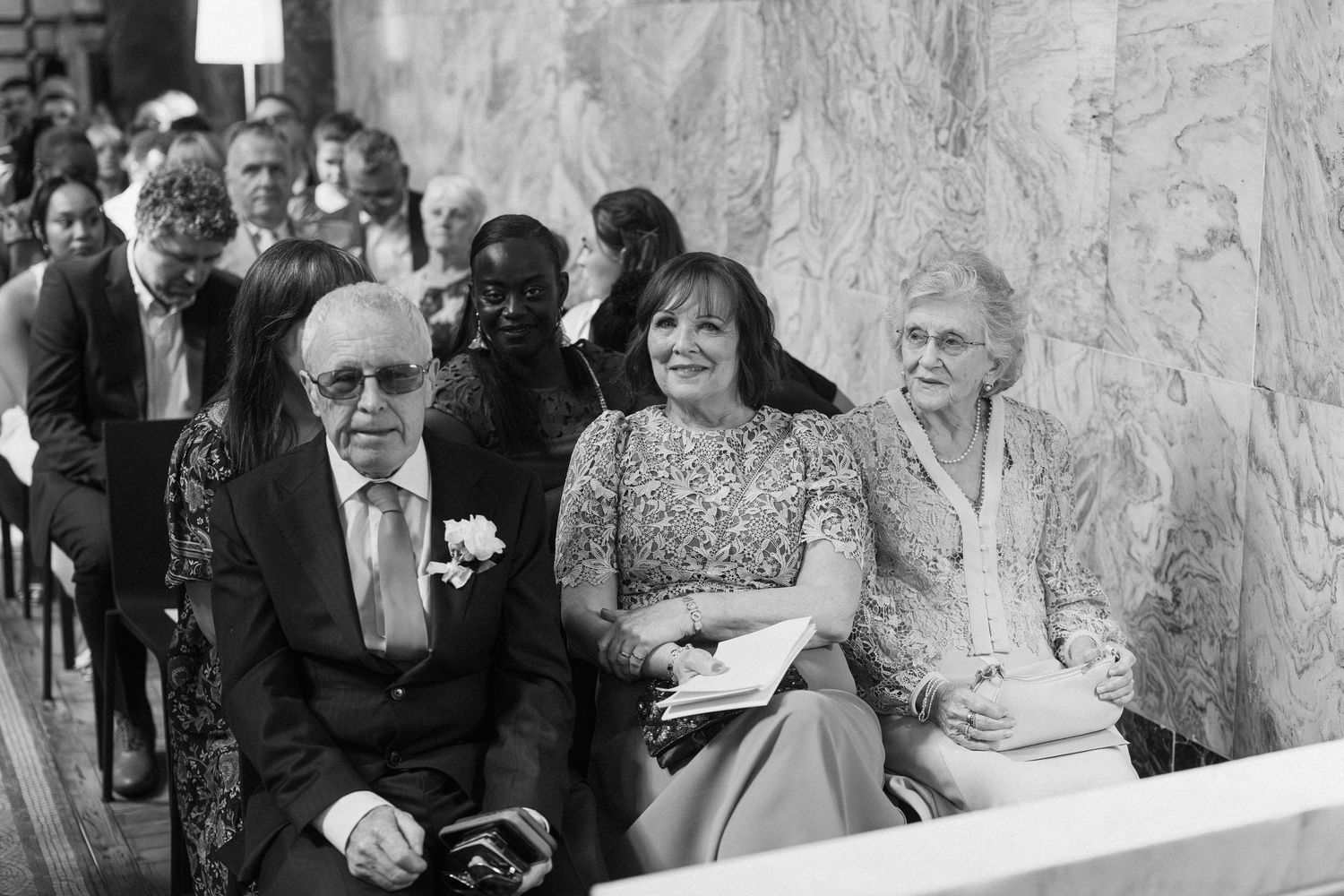 Elderly wedding guests seated in church pews, smiling warmly during a ceremony.
