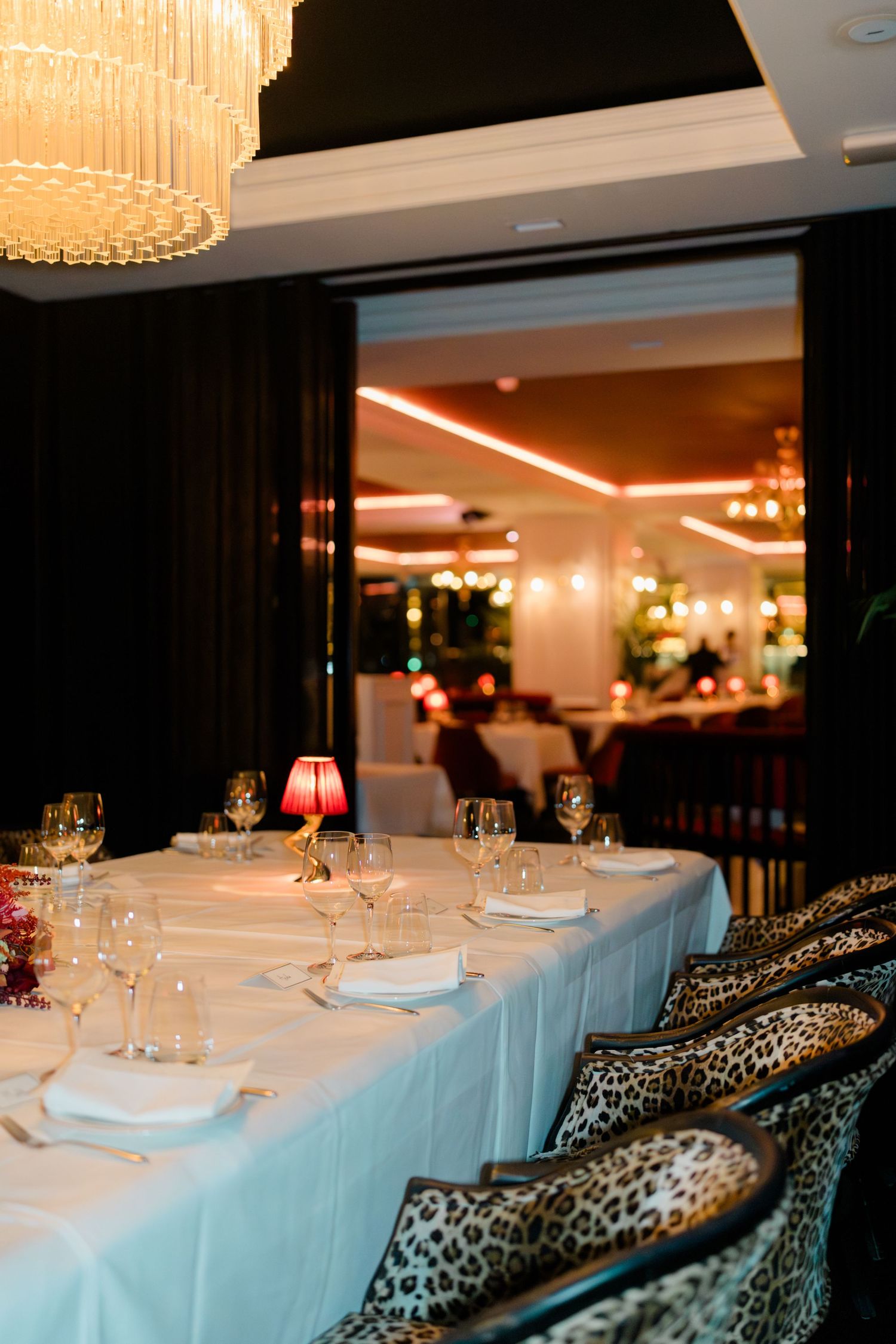 Elegant wedding reception table set with crystal glasses and red lamp under chandelier in restaurant.