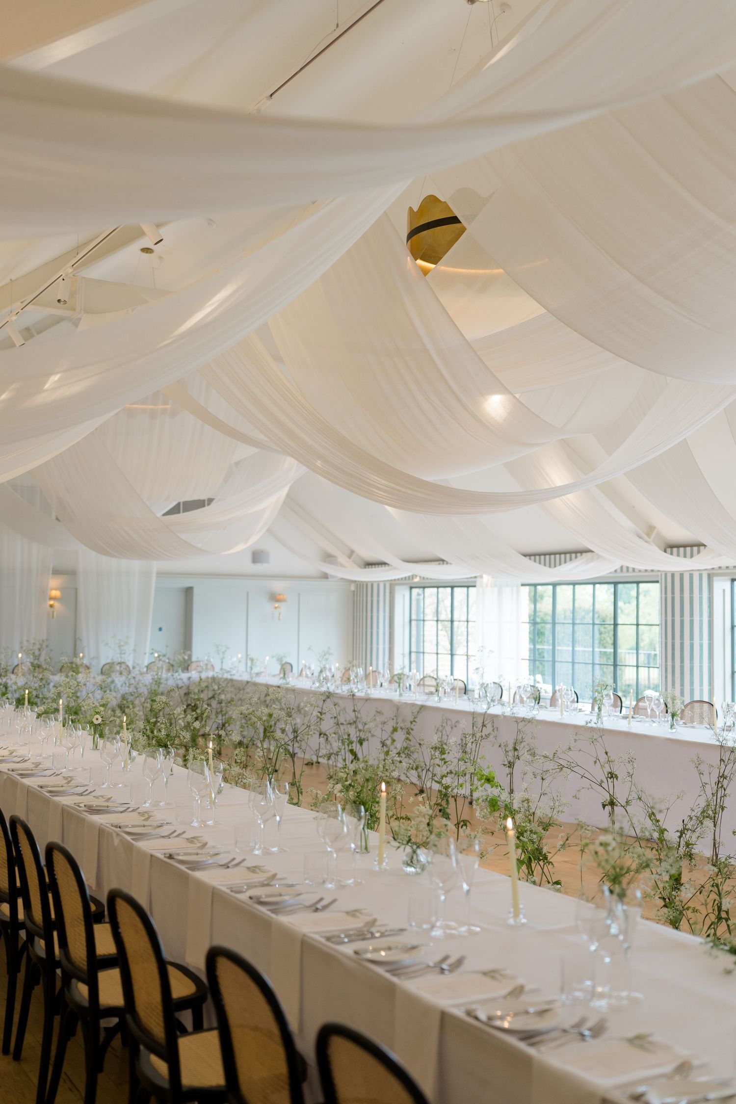 Stunning wedding reception hall with white draped ceiling and long banquet tables adorned with delicate floral centerpieces.