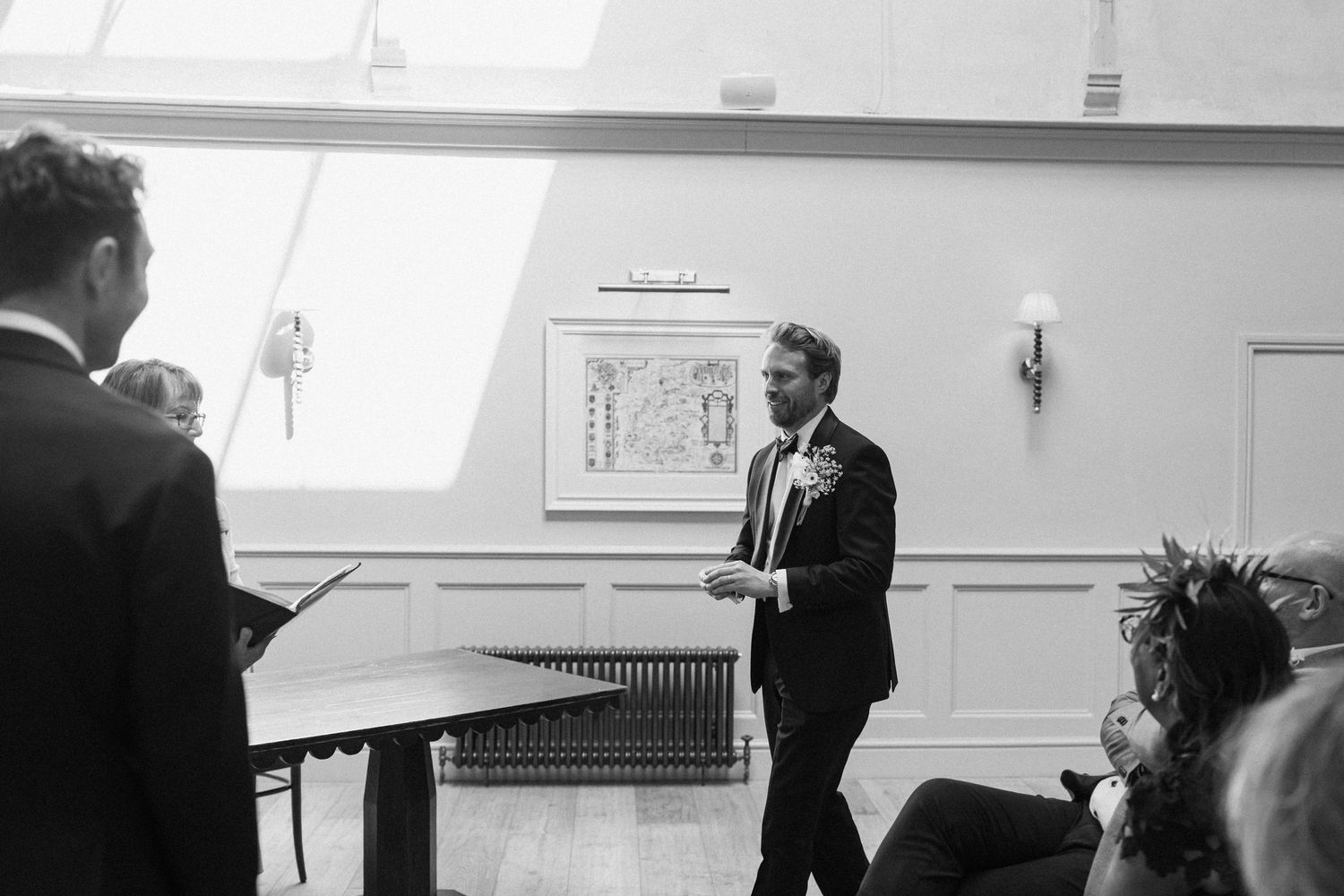 Black and white photo of groom delivering speech at indoor wedding ceremony.