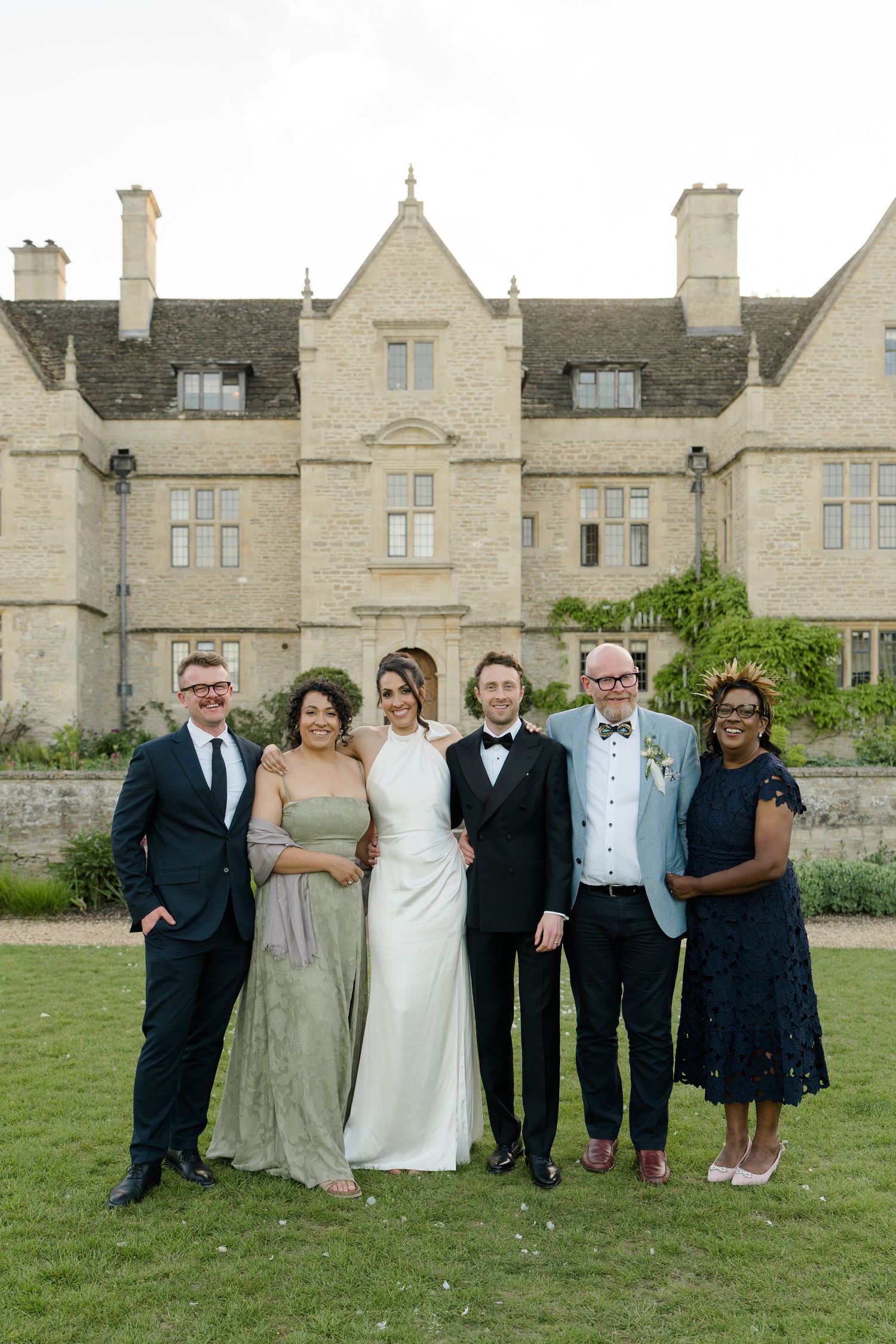 Bride and groom pose with four family members in front of grand stone manor house wedding venue.