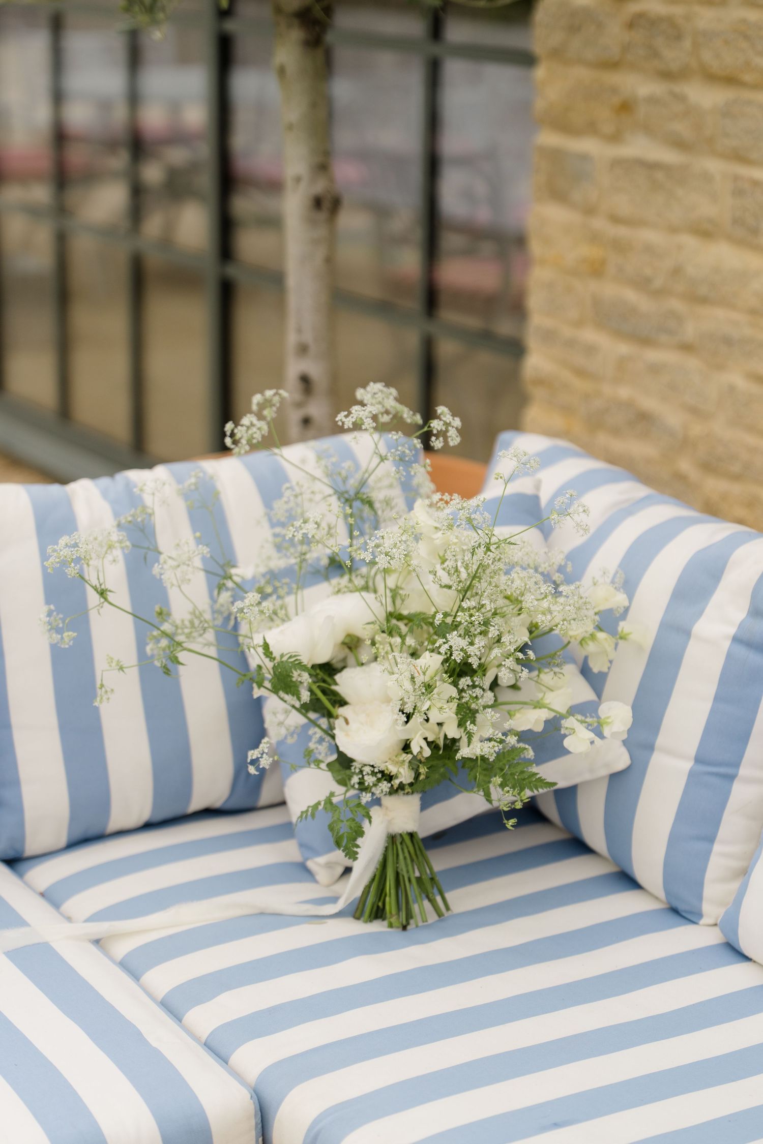 Elegant white wedding bouquet with gypsophila resting on blue and white striped outdoor cushions.