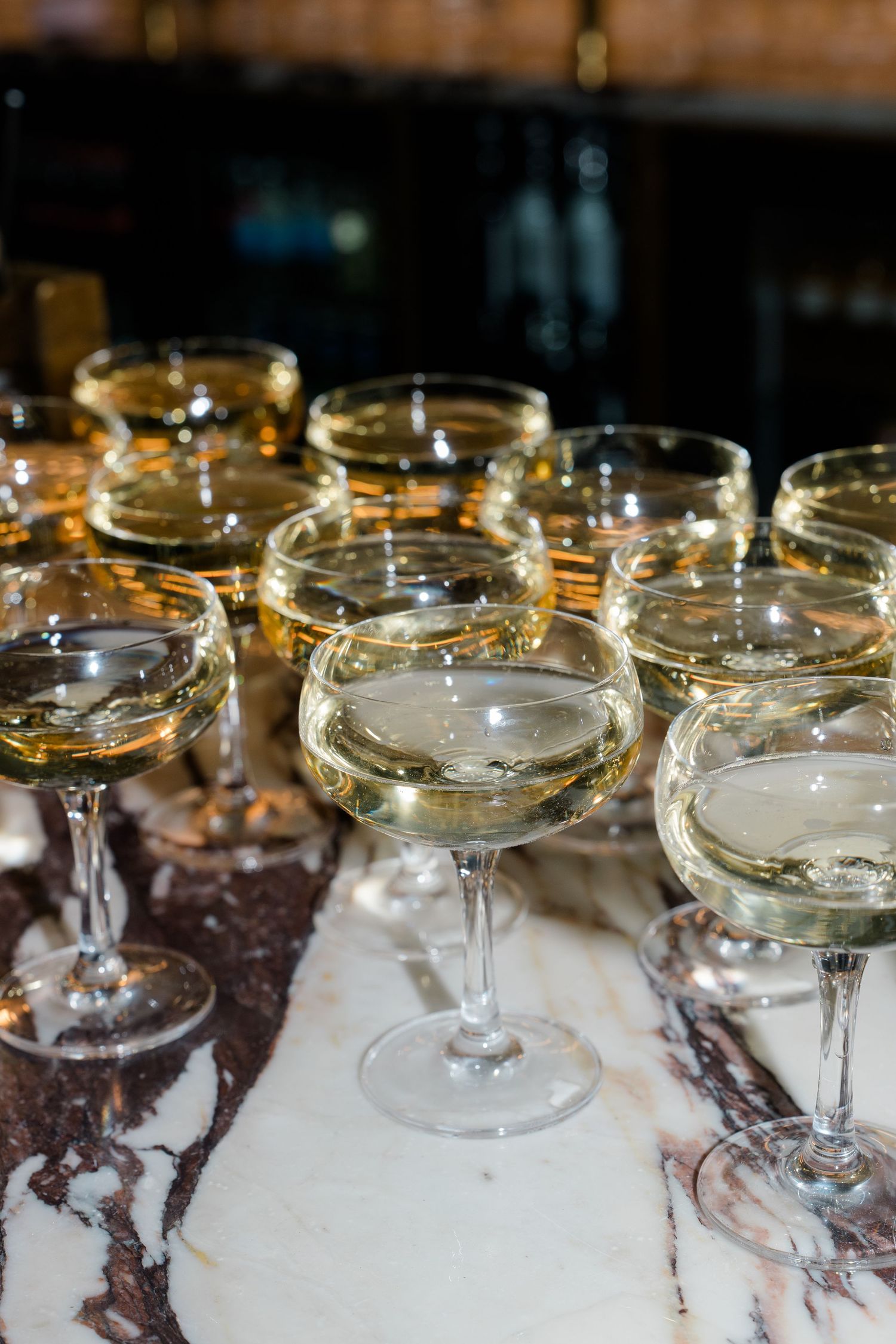 Elegant coupe glasses filled with champagne arranged on a marble bar surface at a wedding.