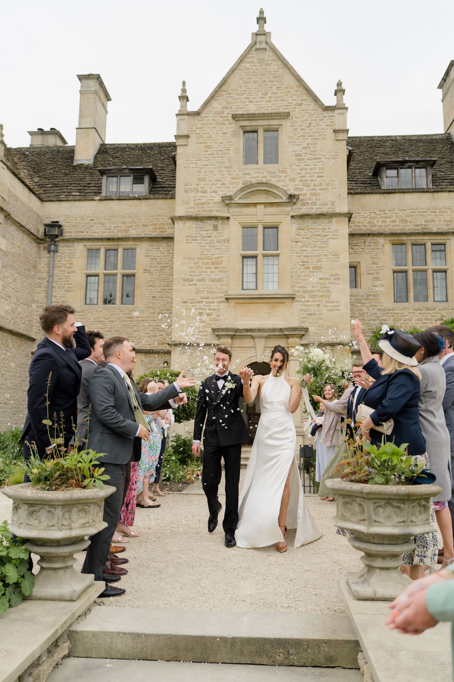 Newlyweds celebrated with confetti outside a grand Cotswolds stone manor house wedding venue.