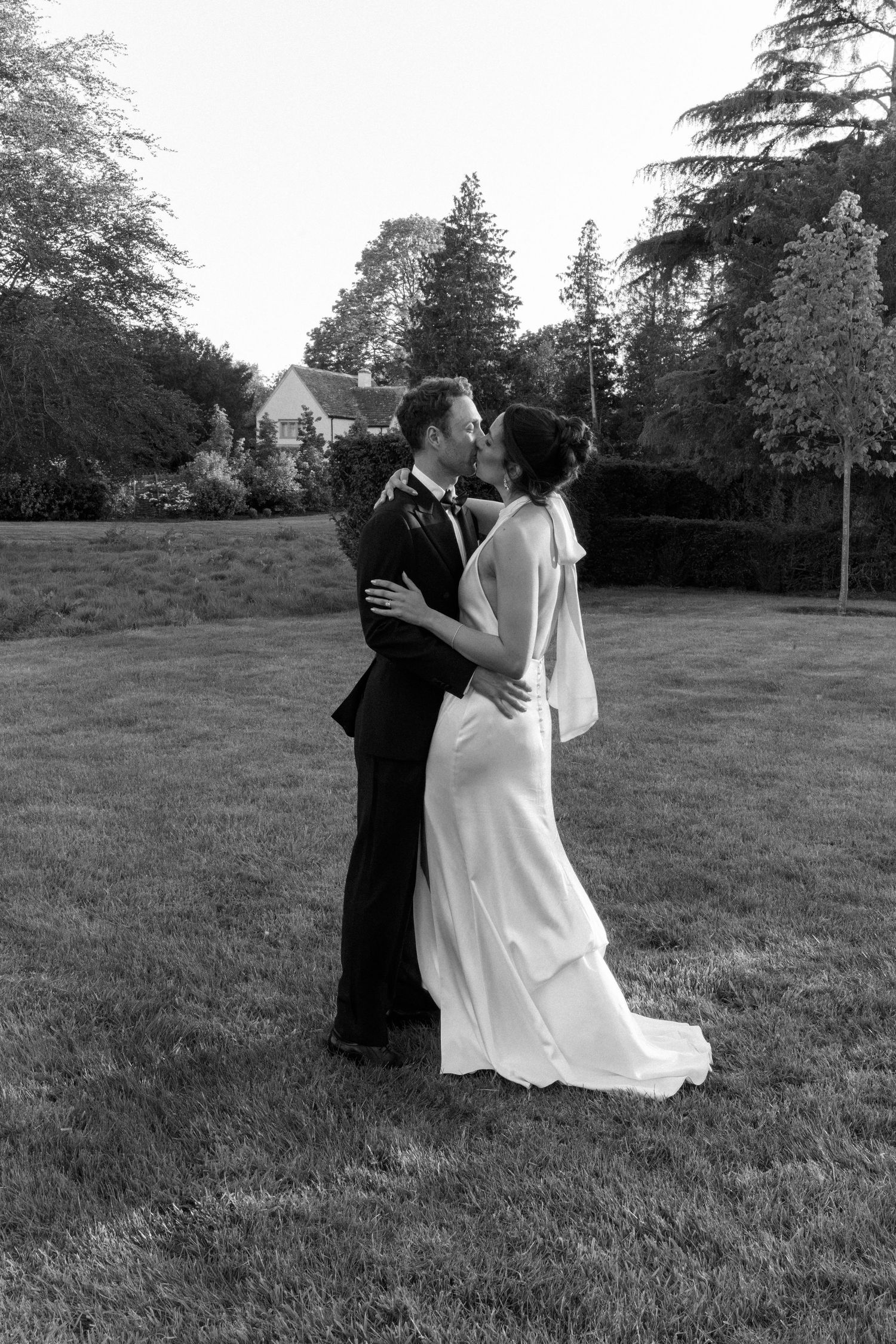 Black and white romantic photo of bride and groom sharing a kiss on expansive lawn at dusk.