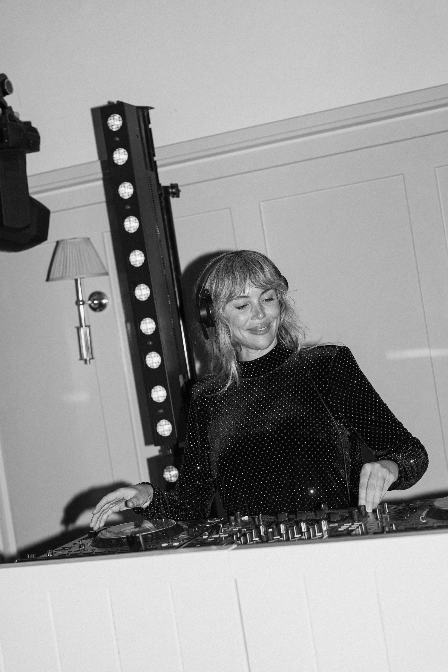 Female DJ performs at wedding reception wearing headphones behind illuminated DJ decks.