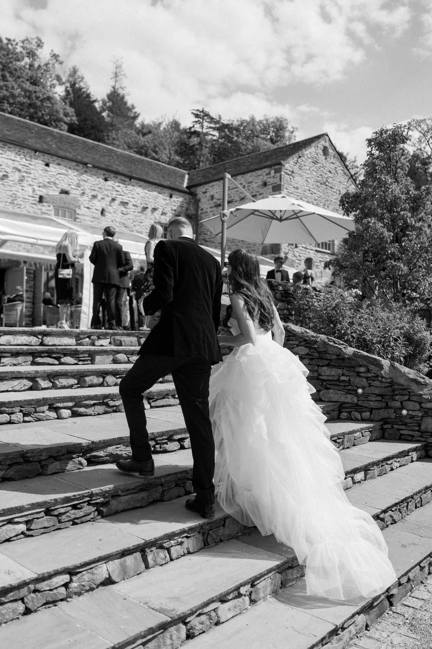 Wedding couple navigates stone steps at an outdoor venue with rustic architecture.