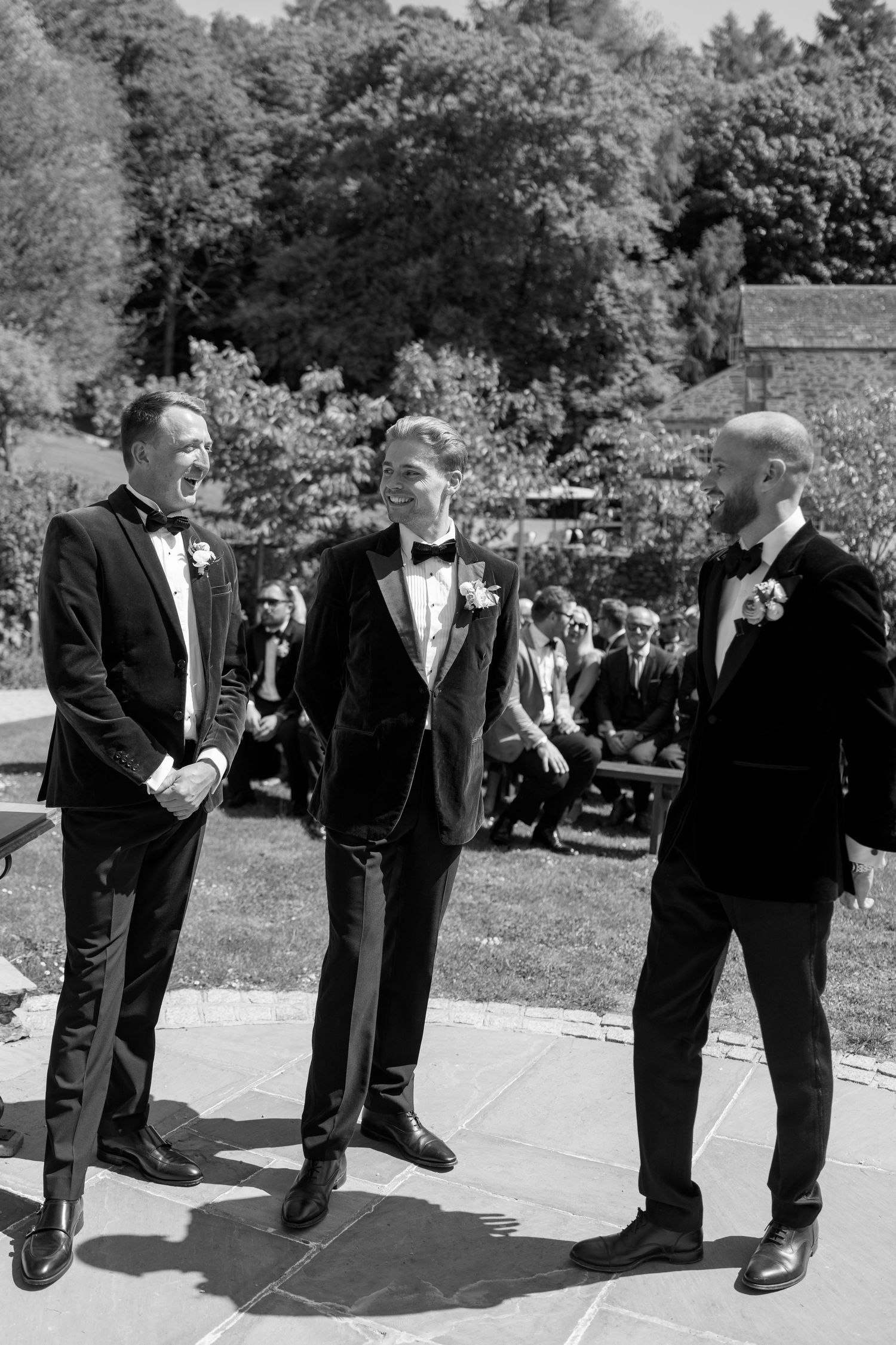Formal wedding guests stand in conversation on a sunny patio.