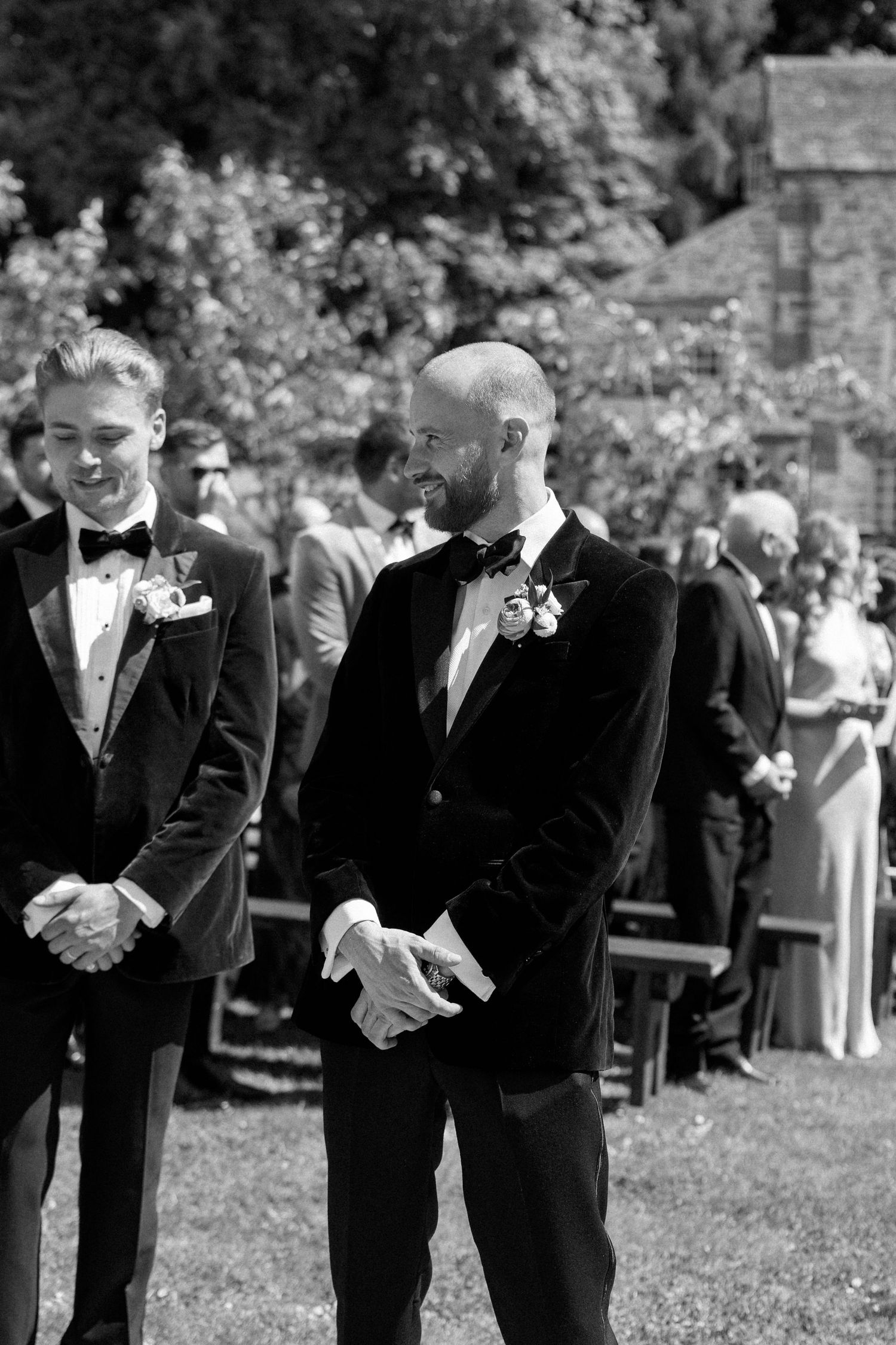 Groomsmen share a lighthearted moment during an outdoor wedding ceremony.