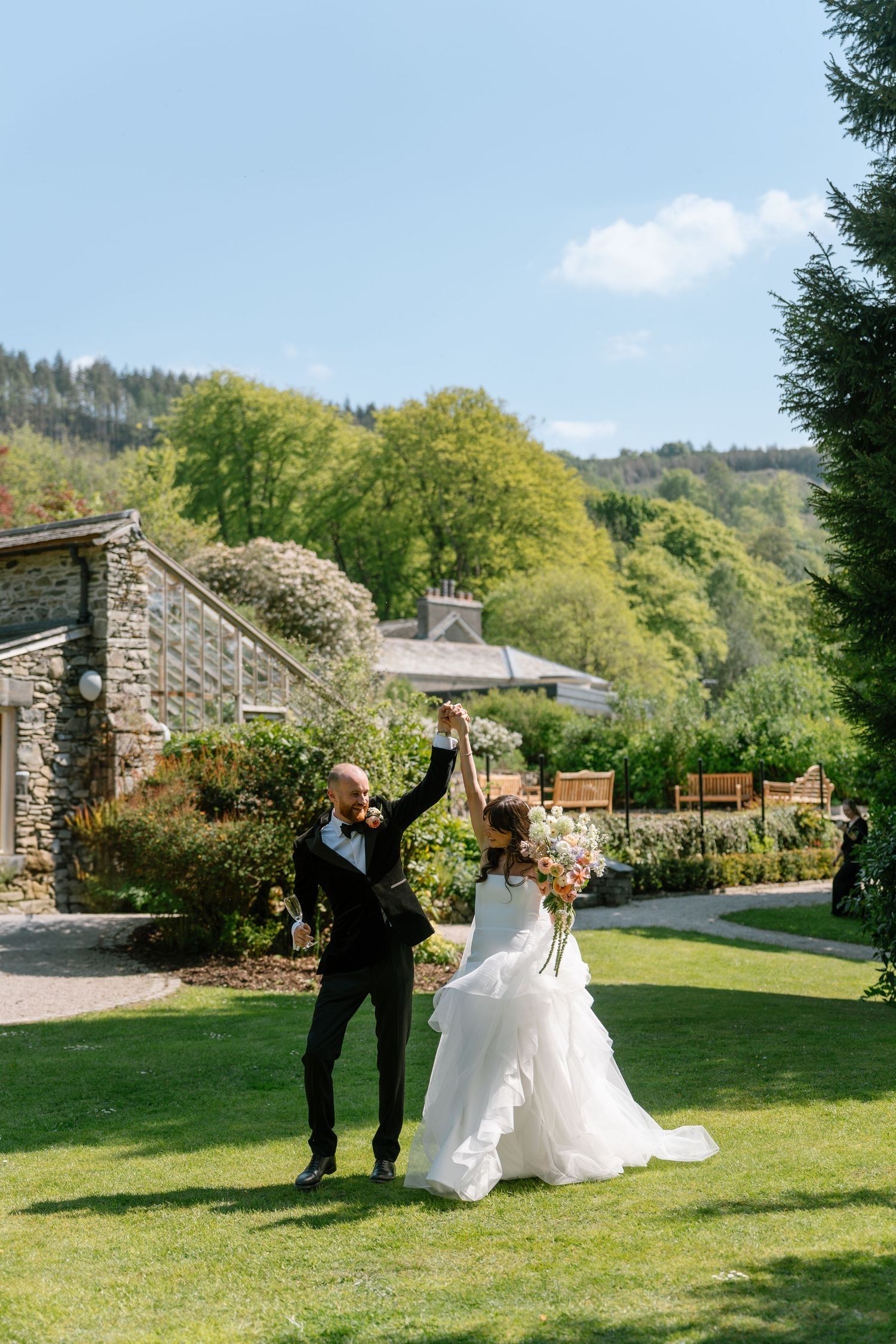 A celebratory moment captured as newlyweds raise their arms in joy on a garden lawn.