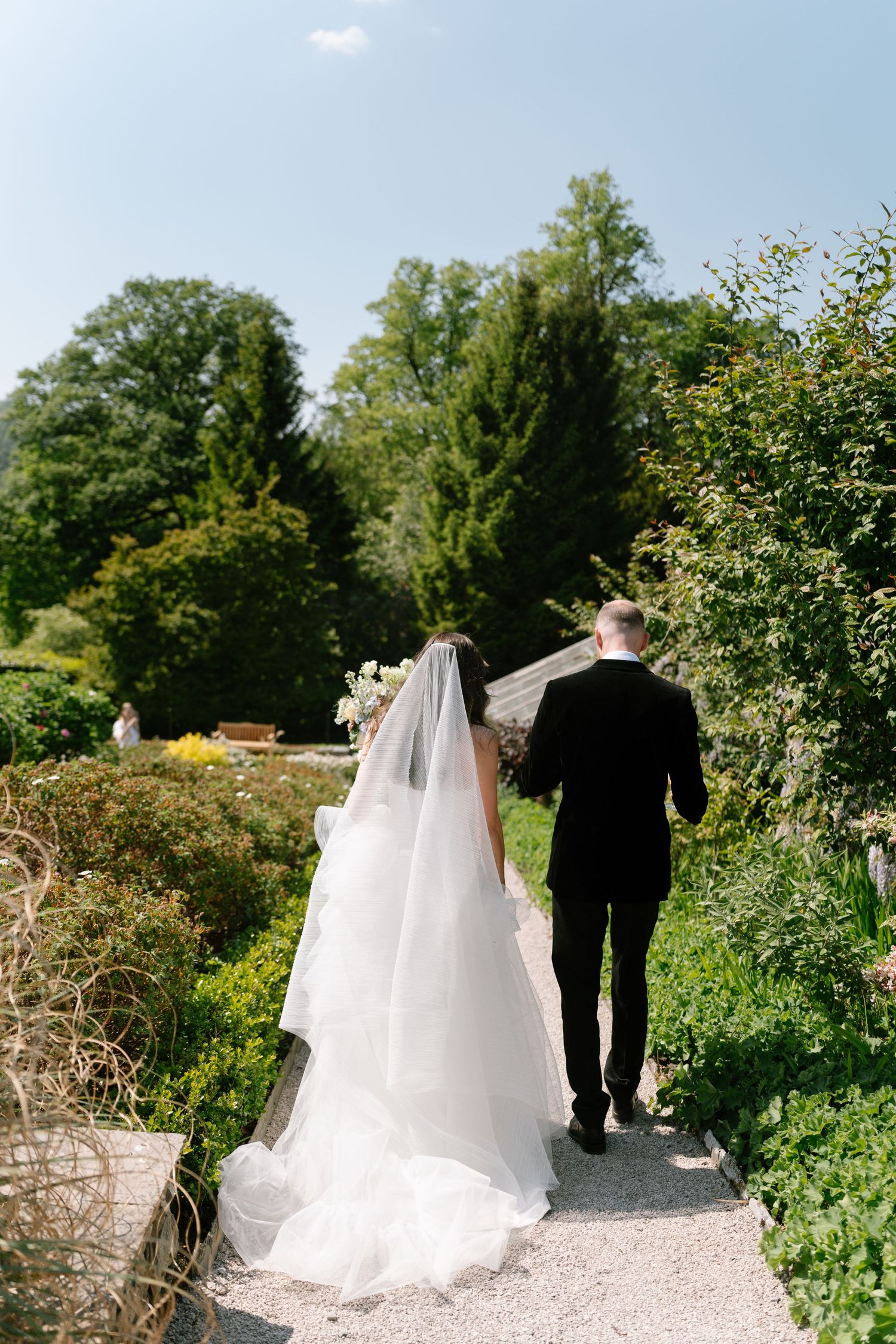 A couple walks down a winding gravel path surrounded by garden landscaping.
