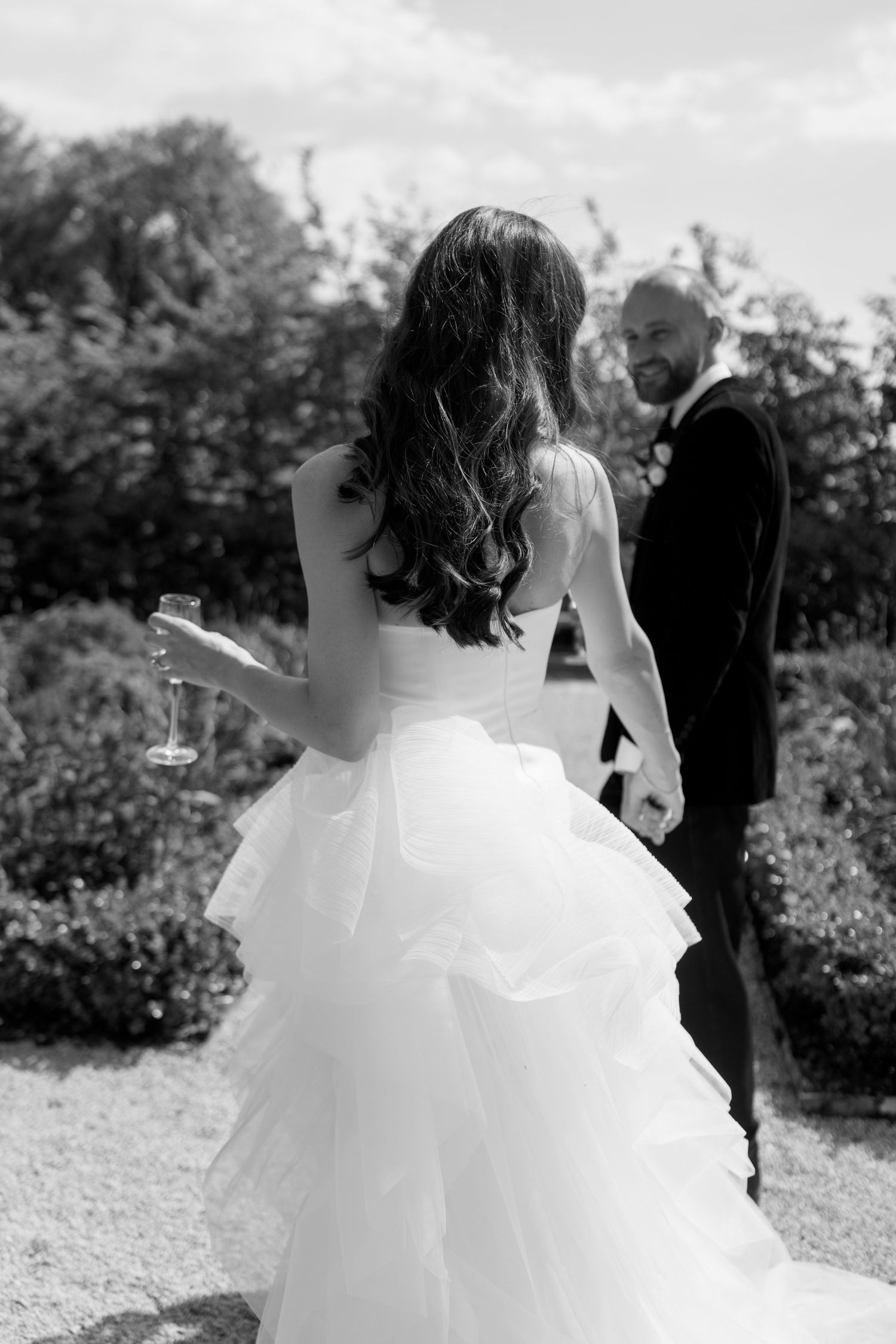 Close-up details of a flowing white wedding dress as couple walks through garden setting.