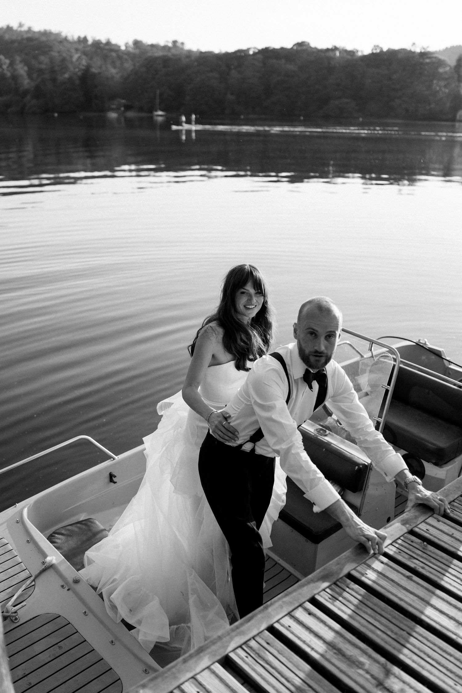 Playful wedding couple sequence climbing onto dock by lake at sunset.