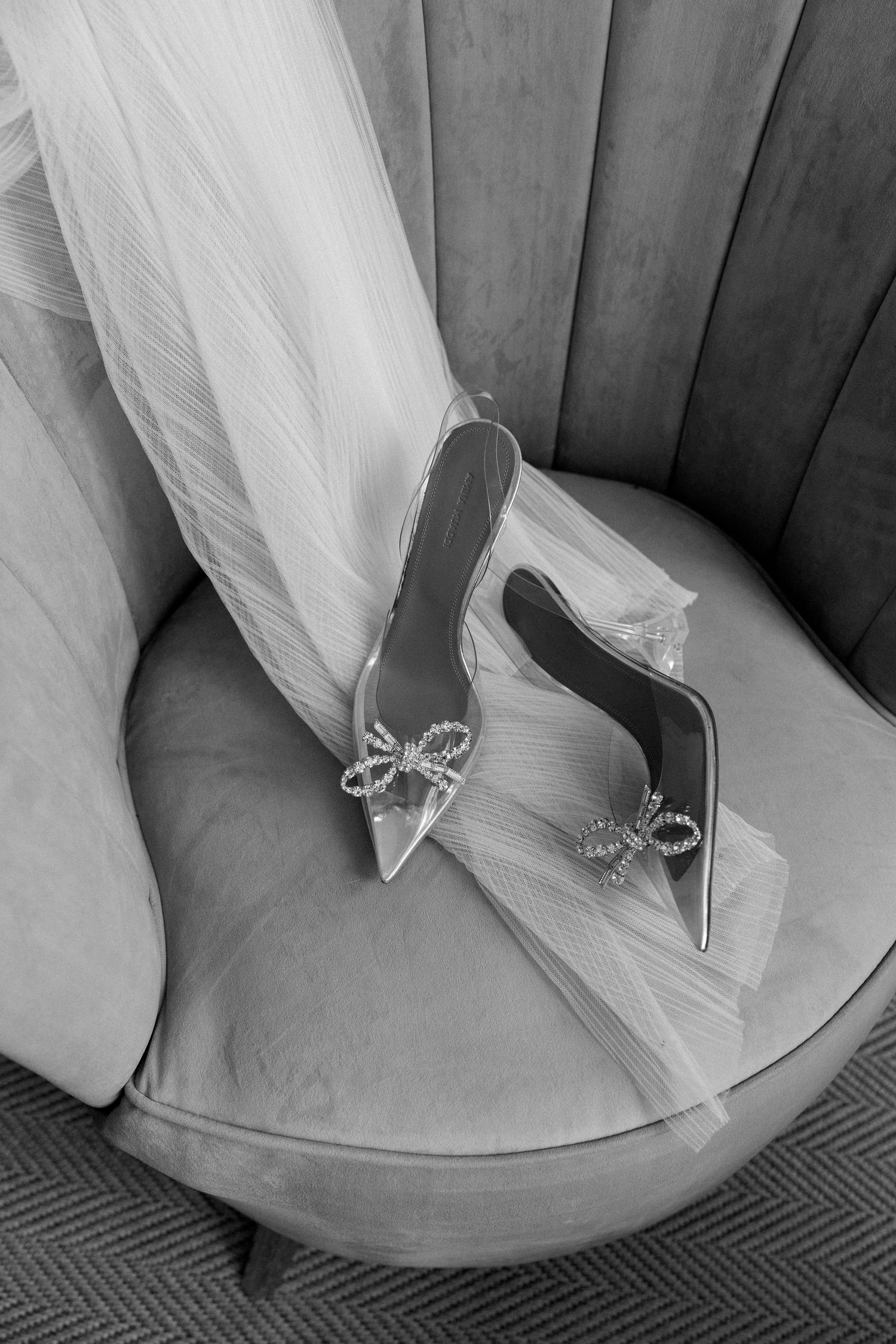 Close-up detail of elegant crystal-embellished bridal shoes against a light colored chair.