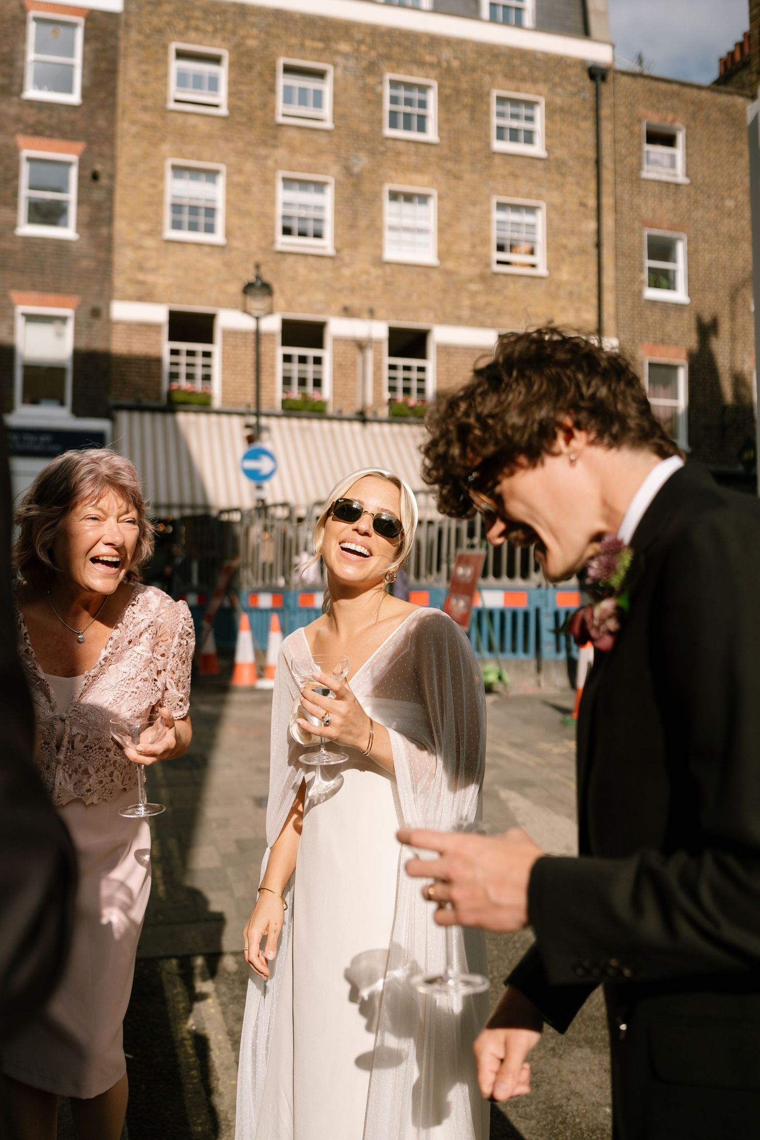 Wedding celebration with guests laughing and drinking in bright sunlight.